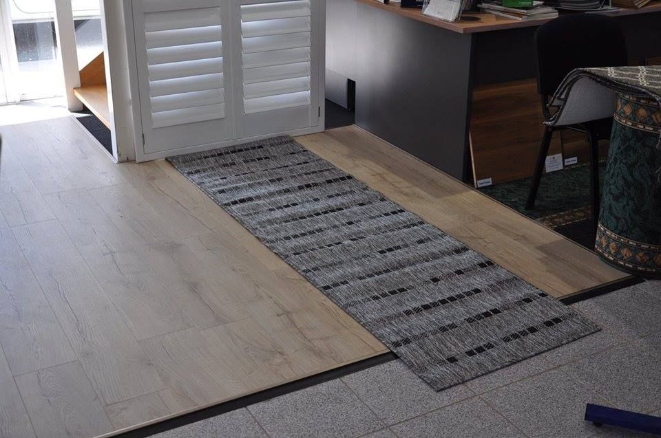 A Rug is Laying on the Floor Next to a Wooden Floor — Bayside Carpets & Flooring in Laurieton, NSW