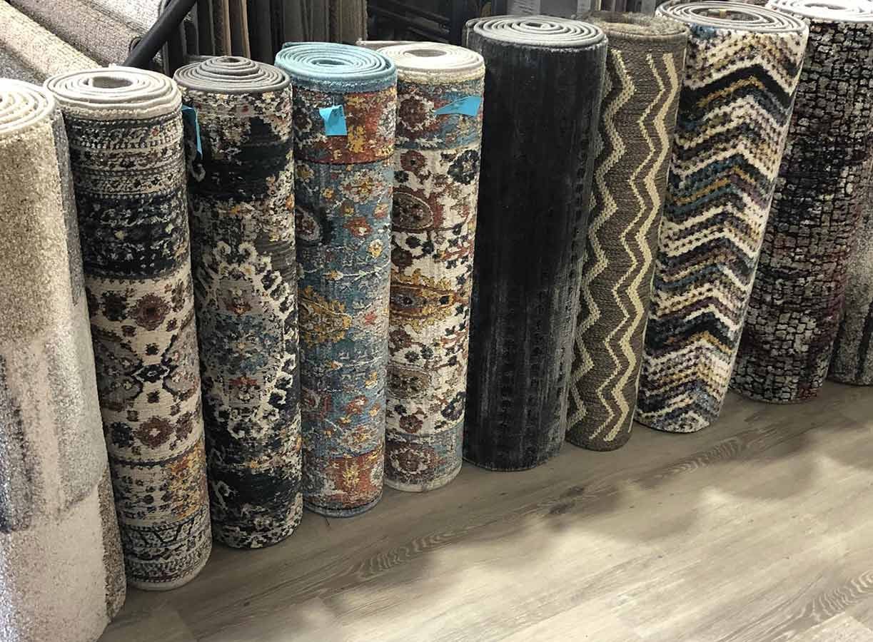 A Bunch of Rolls of Carpet Are Lined Up on a Wooden Floor — Bayside Carpets & Flooring in Laurieton, NSW