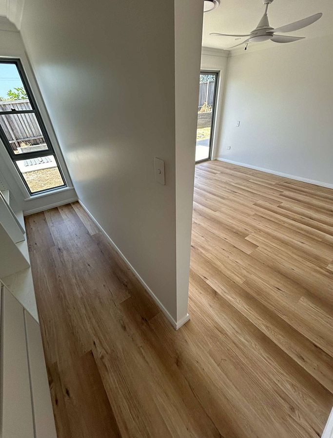 An Empty Room With Hardwood Floors and a Ceiling Fan — Bayside Carpets & Flooring in Harrington, NSW