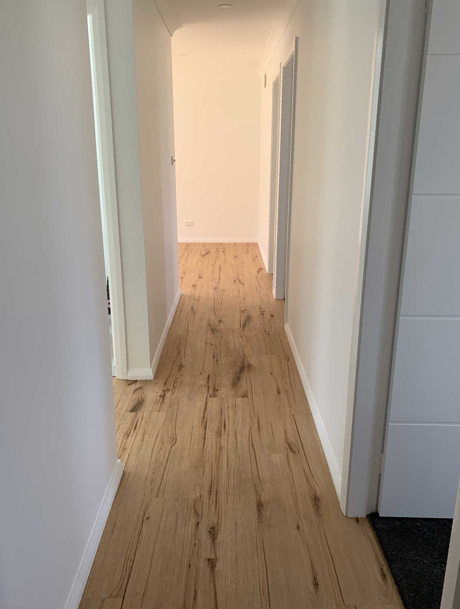 A Long Hallway With Wooden Floors and White Walls — Bayside Carpets & Flooring in Laurieton, NSW