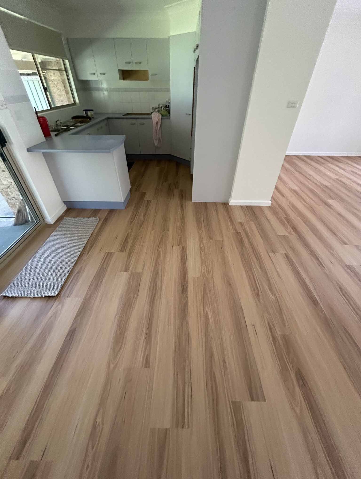 A Kitchen With a Wooden Floor and White Cabinets — Bayside Carpets & Flooring in Port Macquarie, NSW