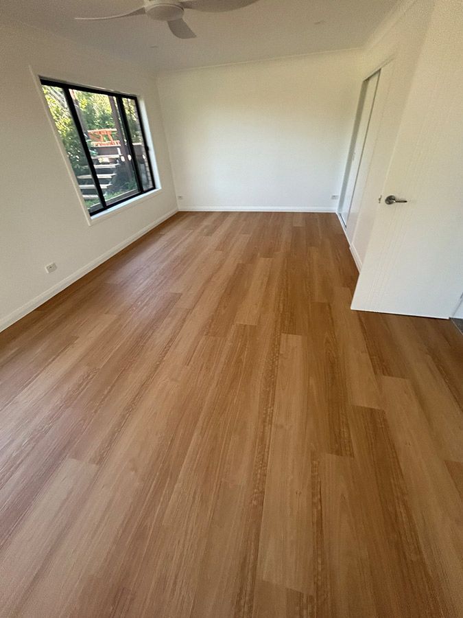 An Empty Room With a Wooden Floor and a Ceiling Fan — Bayside Carpets & Flooring in Port Macquarie, NSW