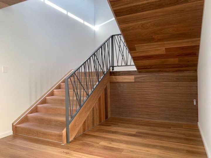 A Wooden Staircase With a Metal Railing in an Empty Room — Bayside Carpets & Flooring in Wauchope, NSW
