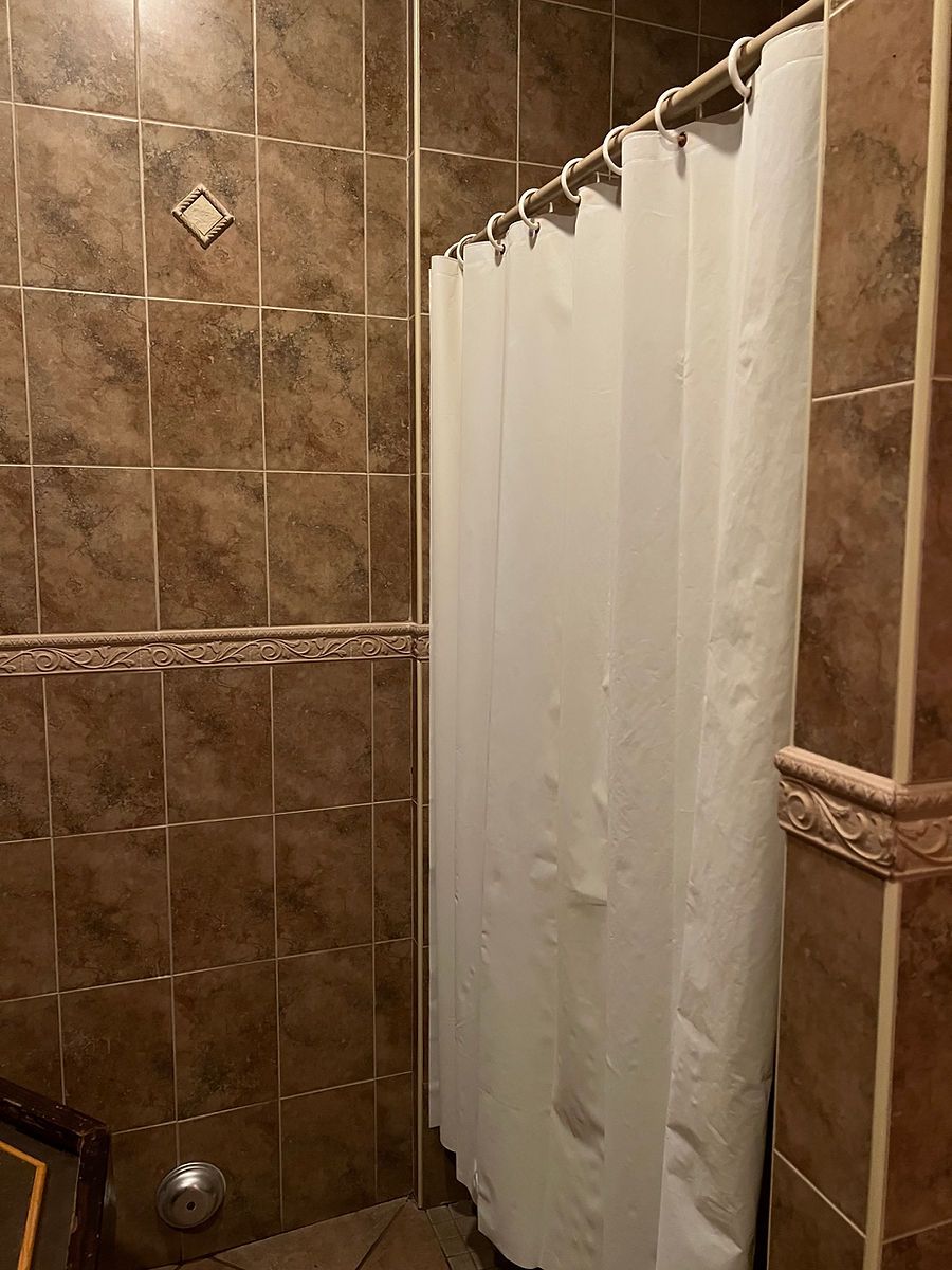 A bathroom with brown tiles and a white shower curtain.
