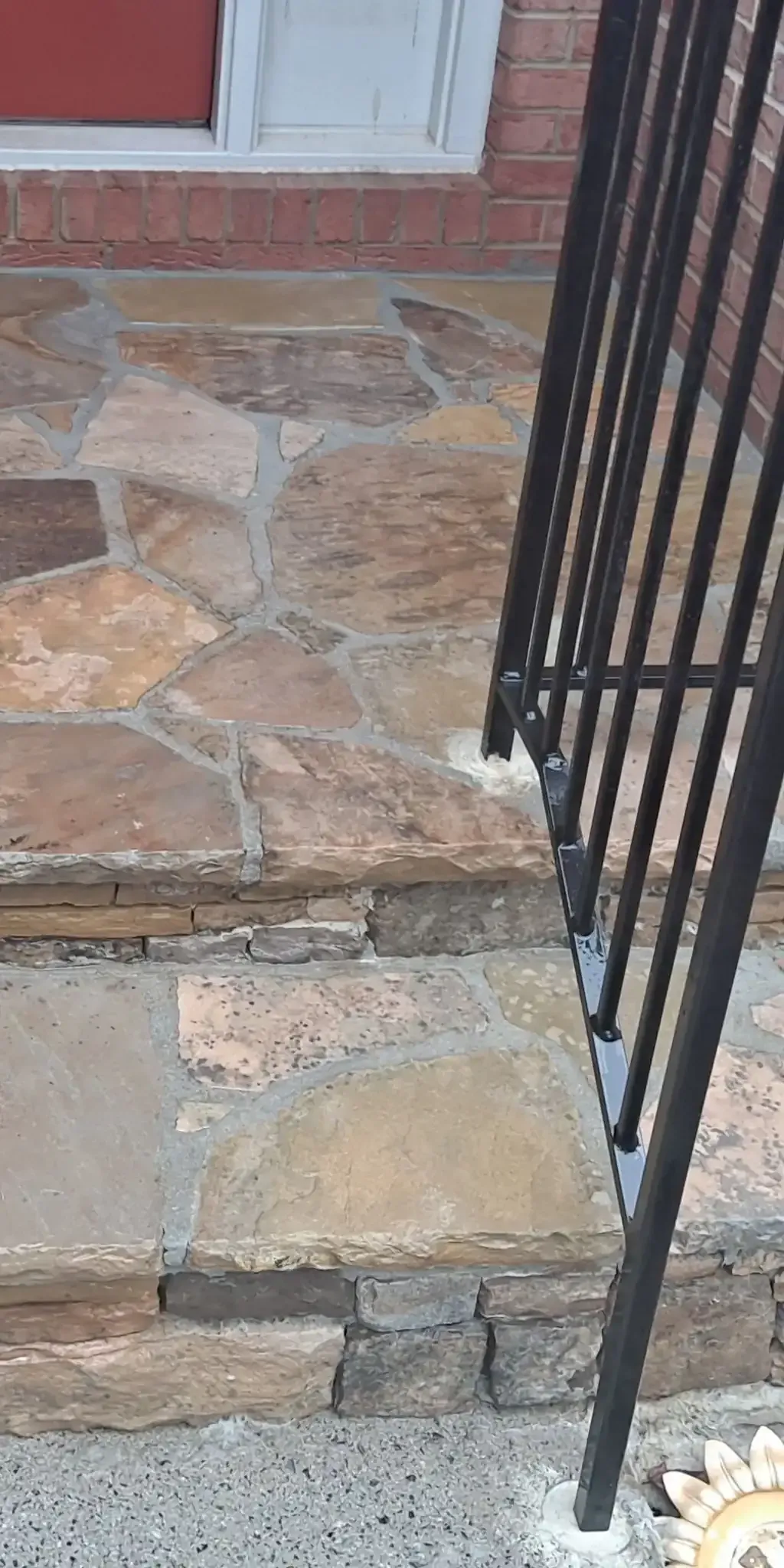 Stone porch steps with a black metal railing beside a brick house entrance