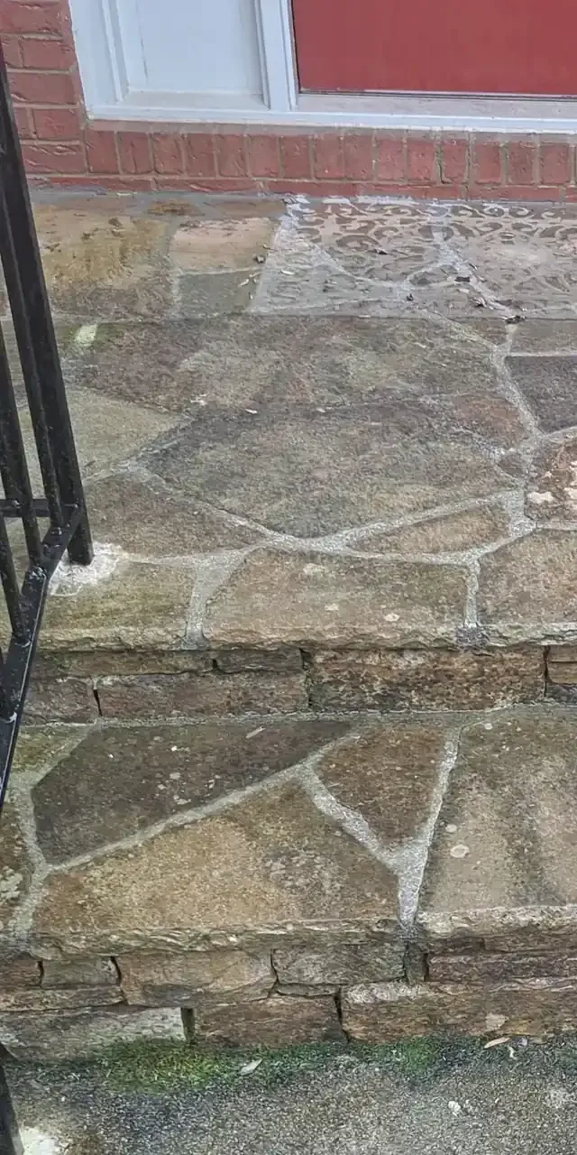 Cracked stone steps leading to a red-brick porch with a black railing