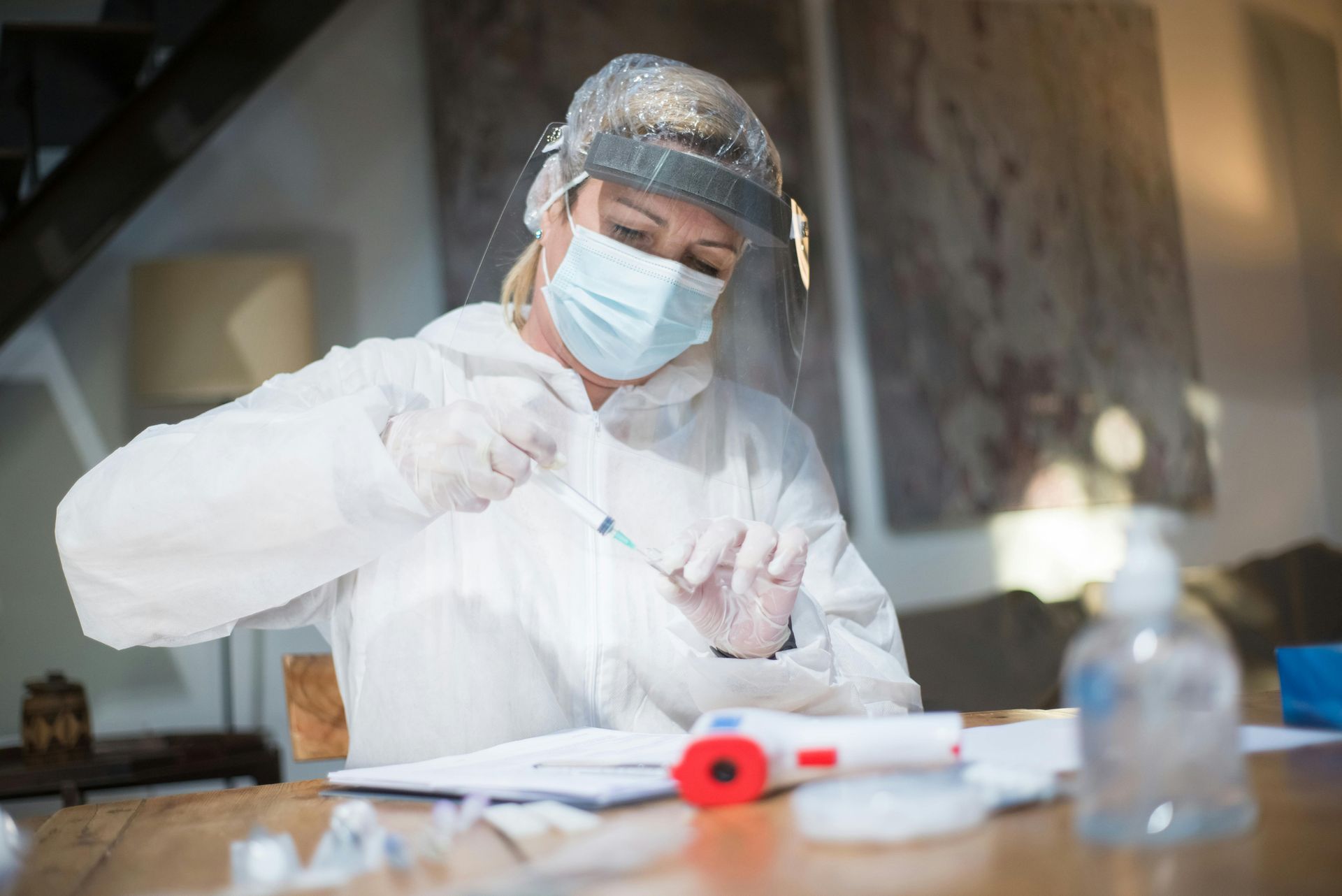 A nurse wearing a mask and gloves is preparing a syringe.
