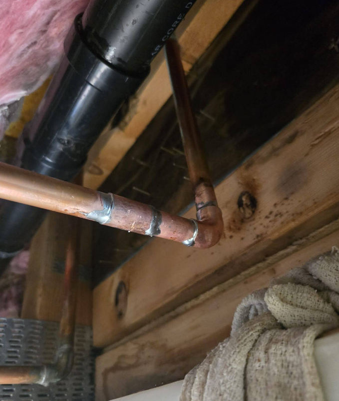 Copper pipes with soldered joints against wood, near a black pipe and insulation.