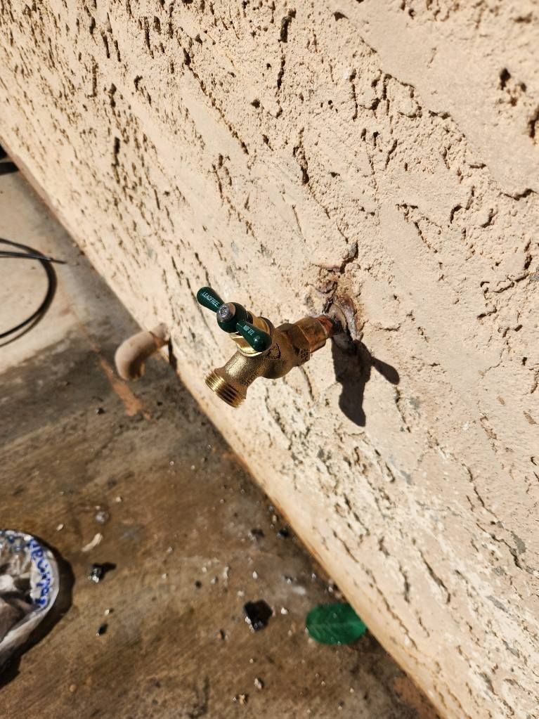 Outdoor spigot attached to a textured beige stucco wall. The spigot is rusty and green.