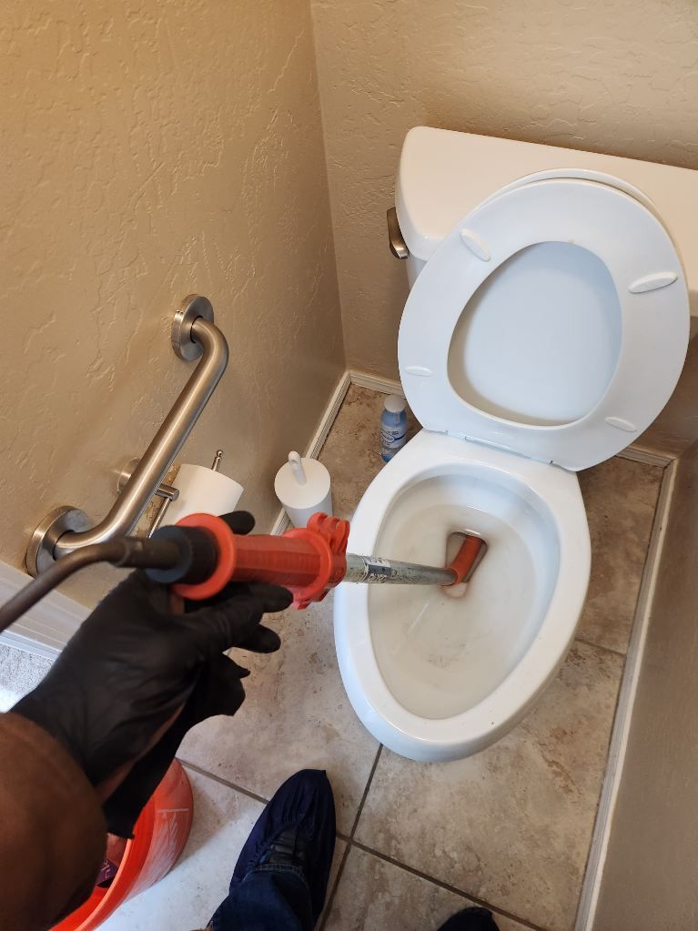 Person unclogging a toilet with a plunger in a bathroom.