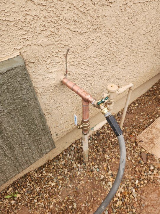 Copper pipes with hose connection on a beige stucco wall, near small stones.