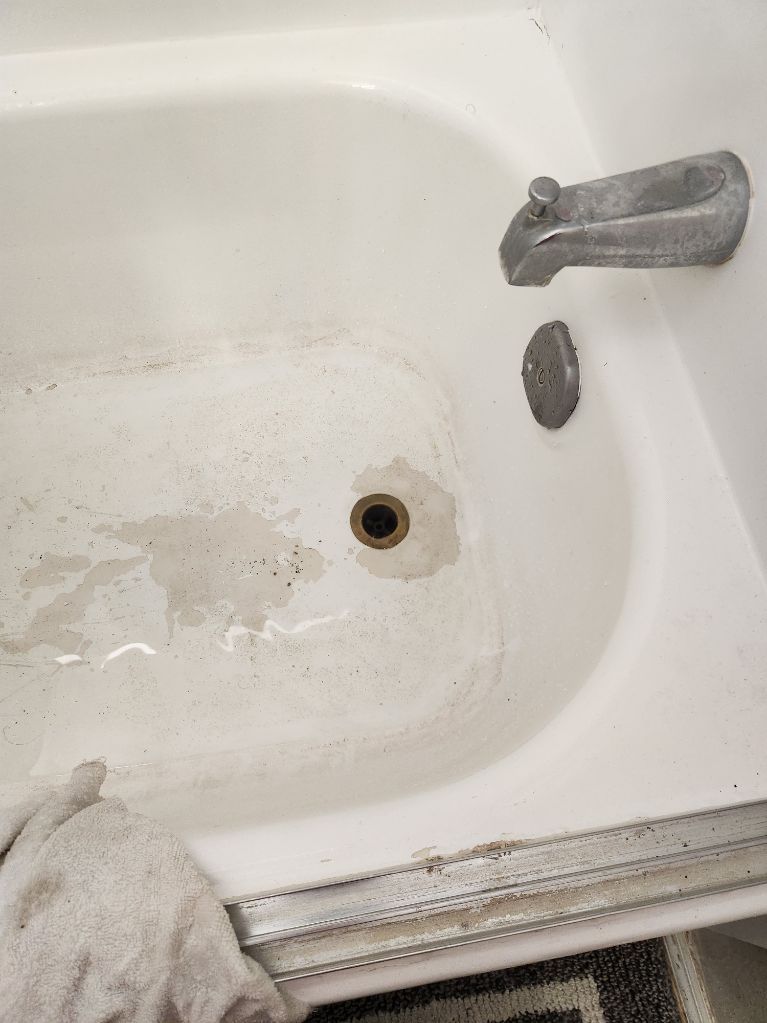 White bathtub with dirty water, drain visible, and faucet. A cloth lies on the edge.