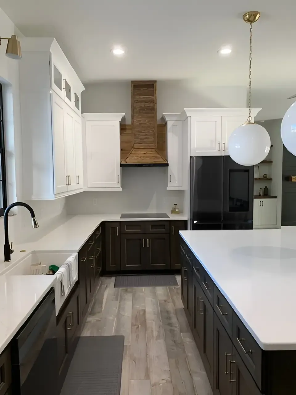 A modern kitchen with dark lower cabinets, white upper cabinets, a wooden range hood, and a large white island.