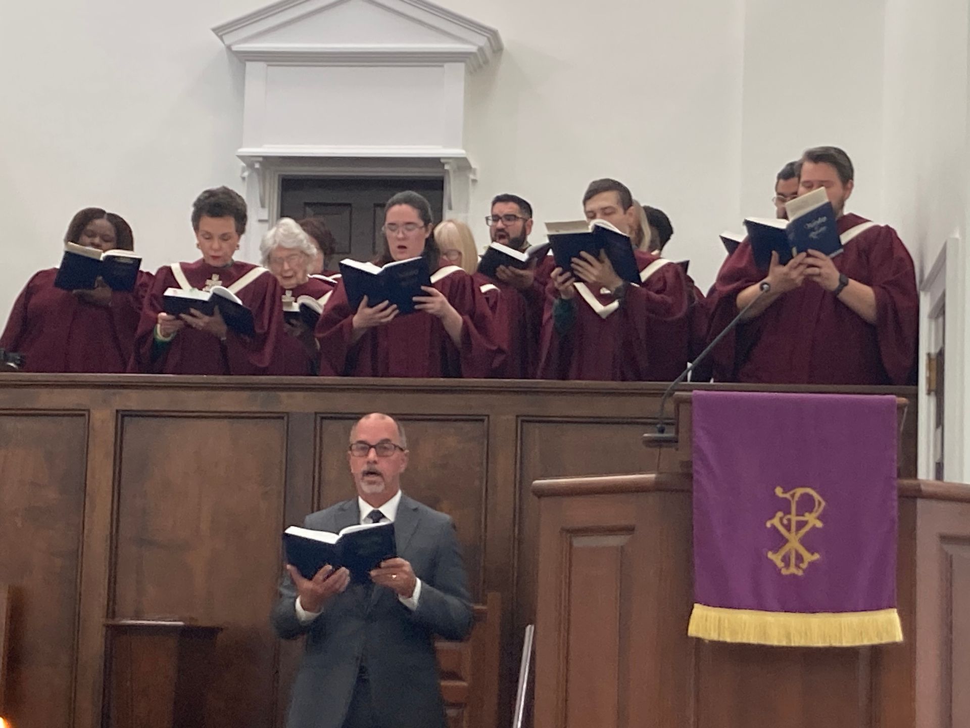 A choir is singing in a church with a man standing behind them.