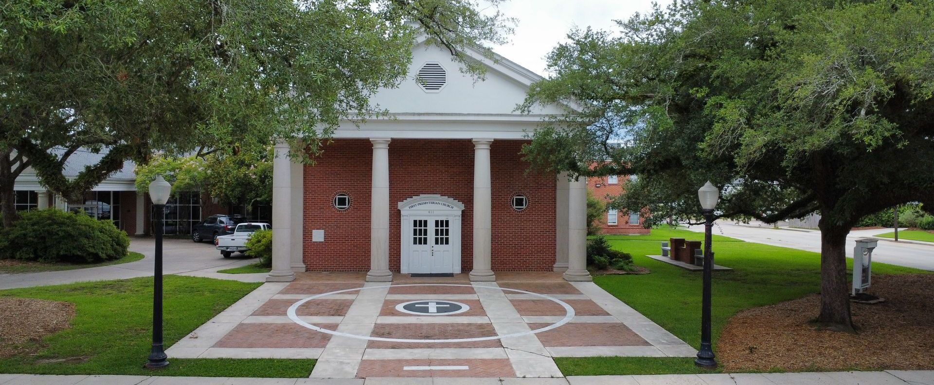 A large brick building with columns and a white door is surrounded by trees.