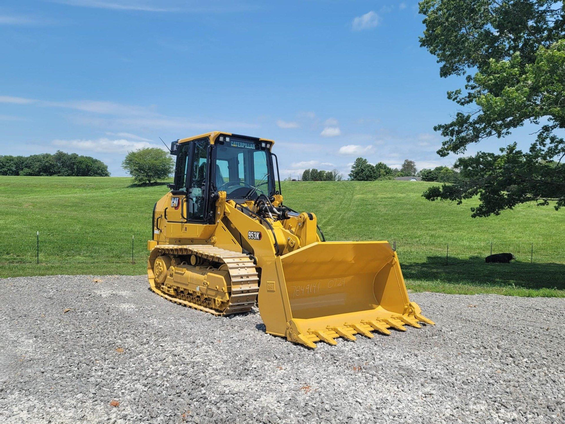 A yellow bulldozer is parked in a gravel lot in front of a grassy field.