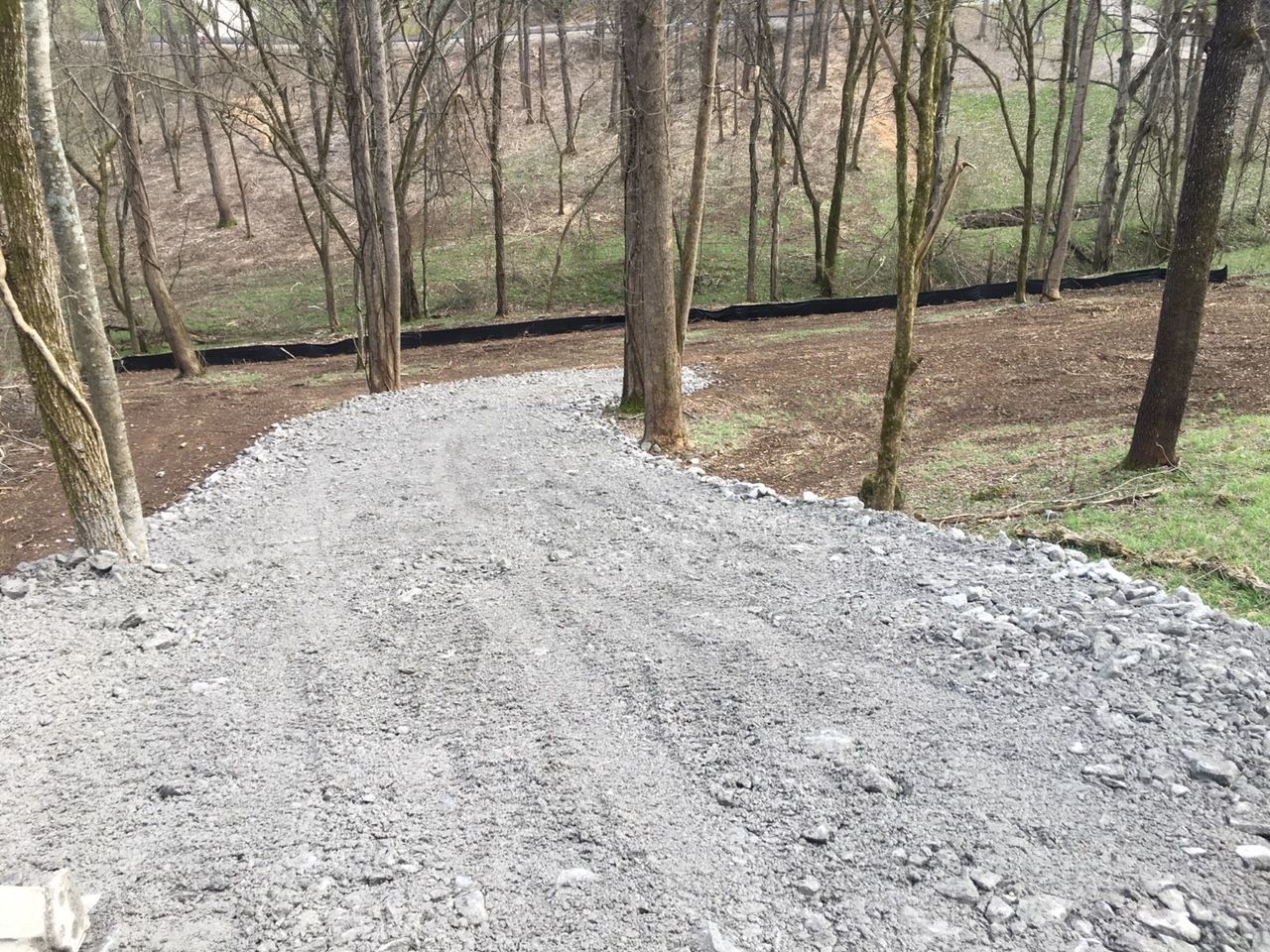 A gravel road going through a forest with trees on both sides.
