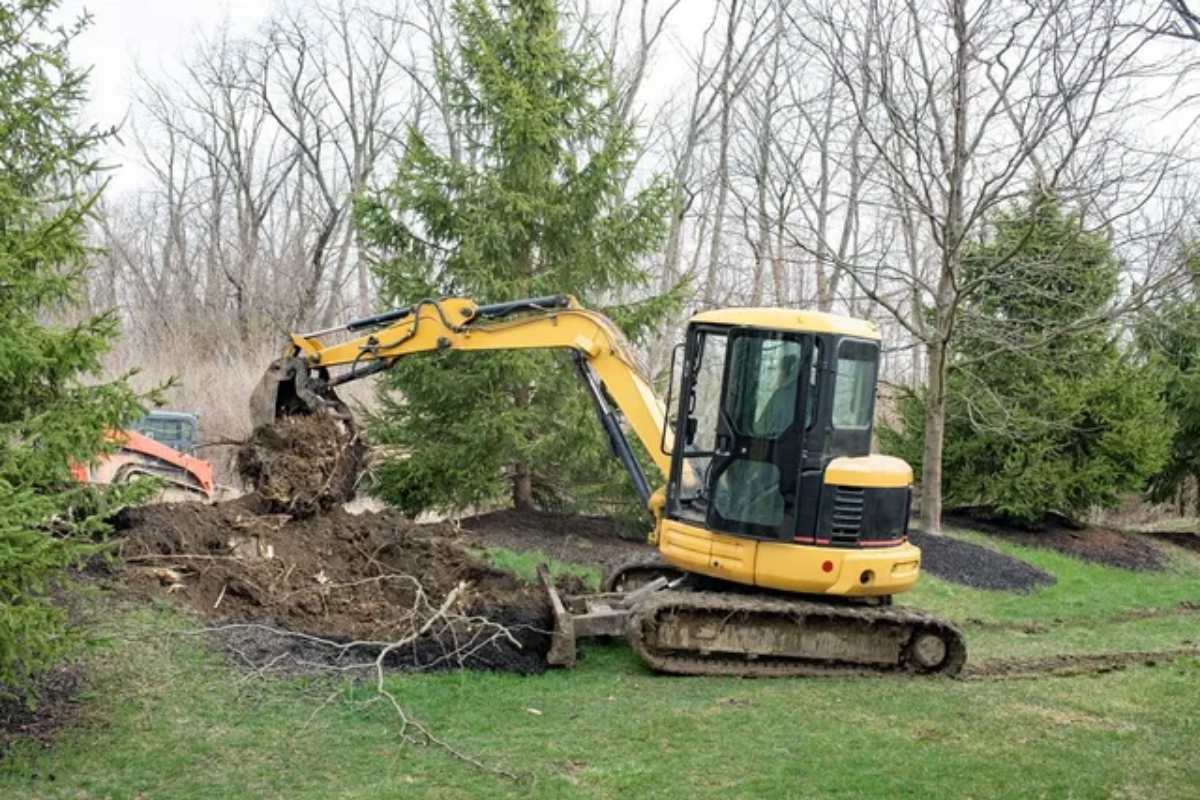 A yellow excavator is digging a hole in a yard.