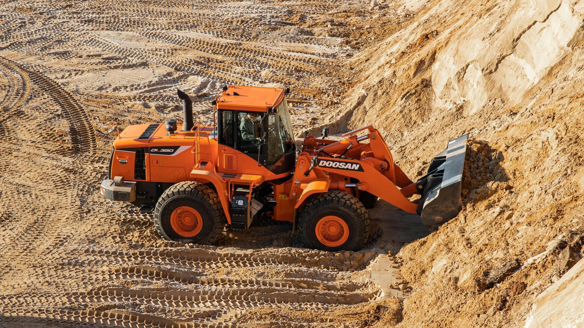 An orange wheel loader is driving through a pile of dirt.