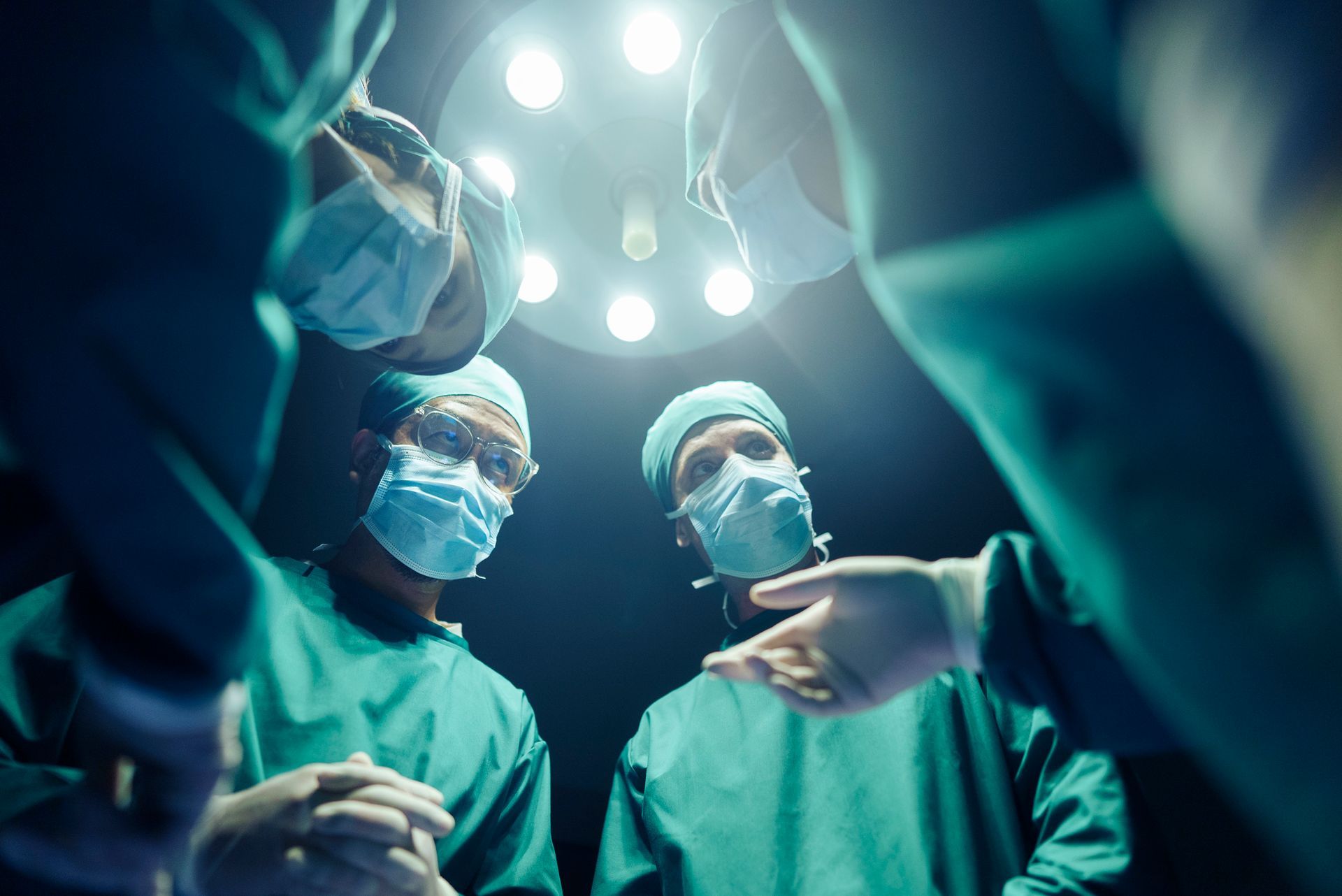 Two surgeons are looking up at a light in an operating room.