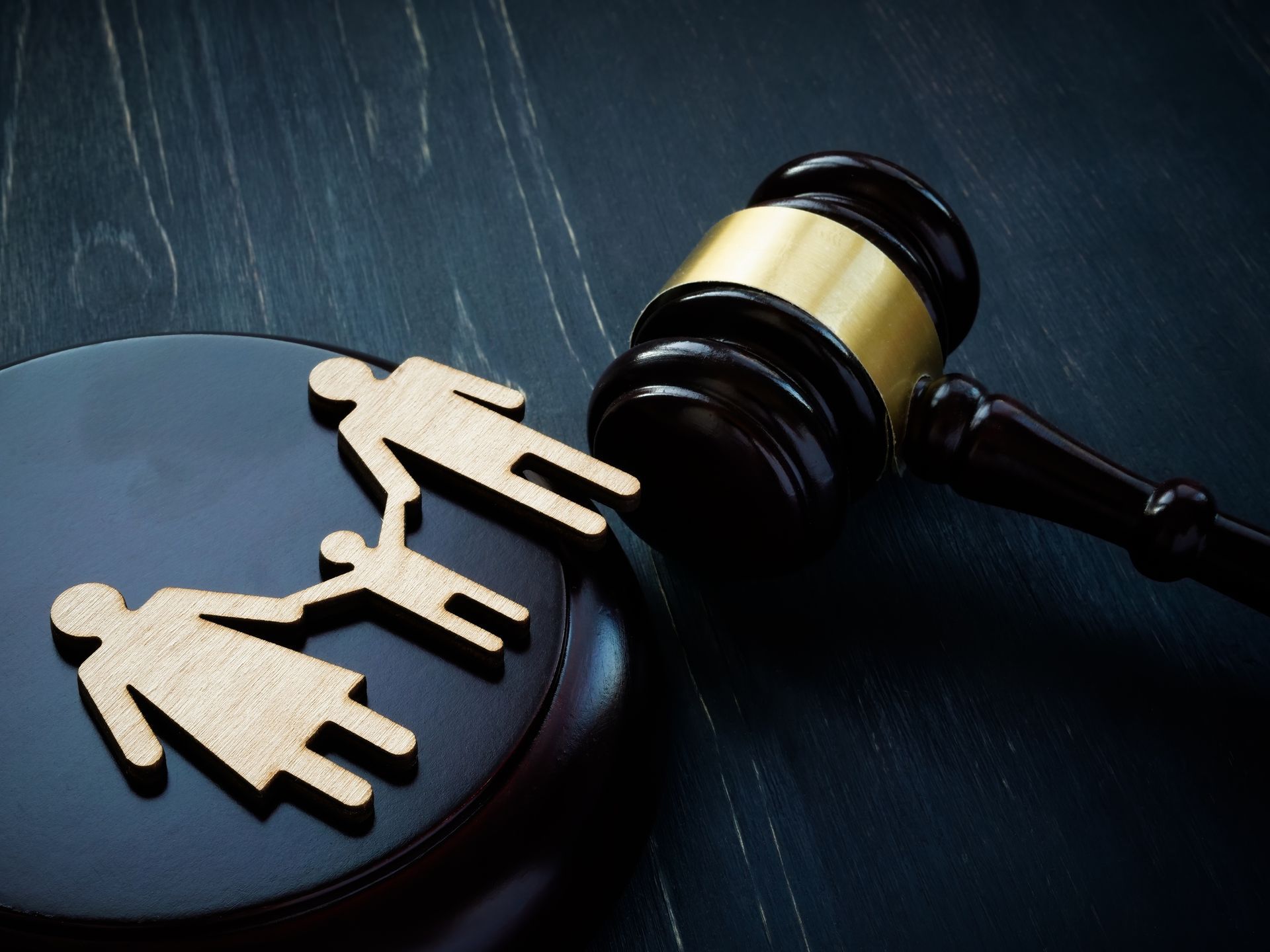 A  wooden family figure and a court hammer in a dark desk, from a child custody law firm.