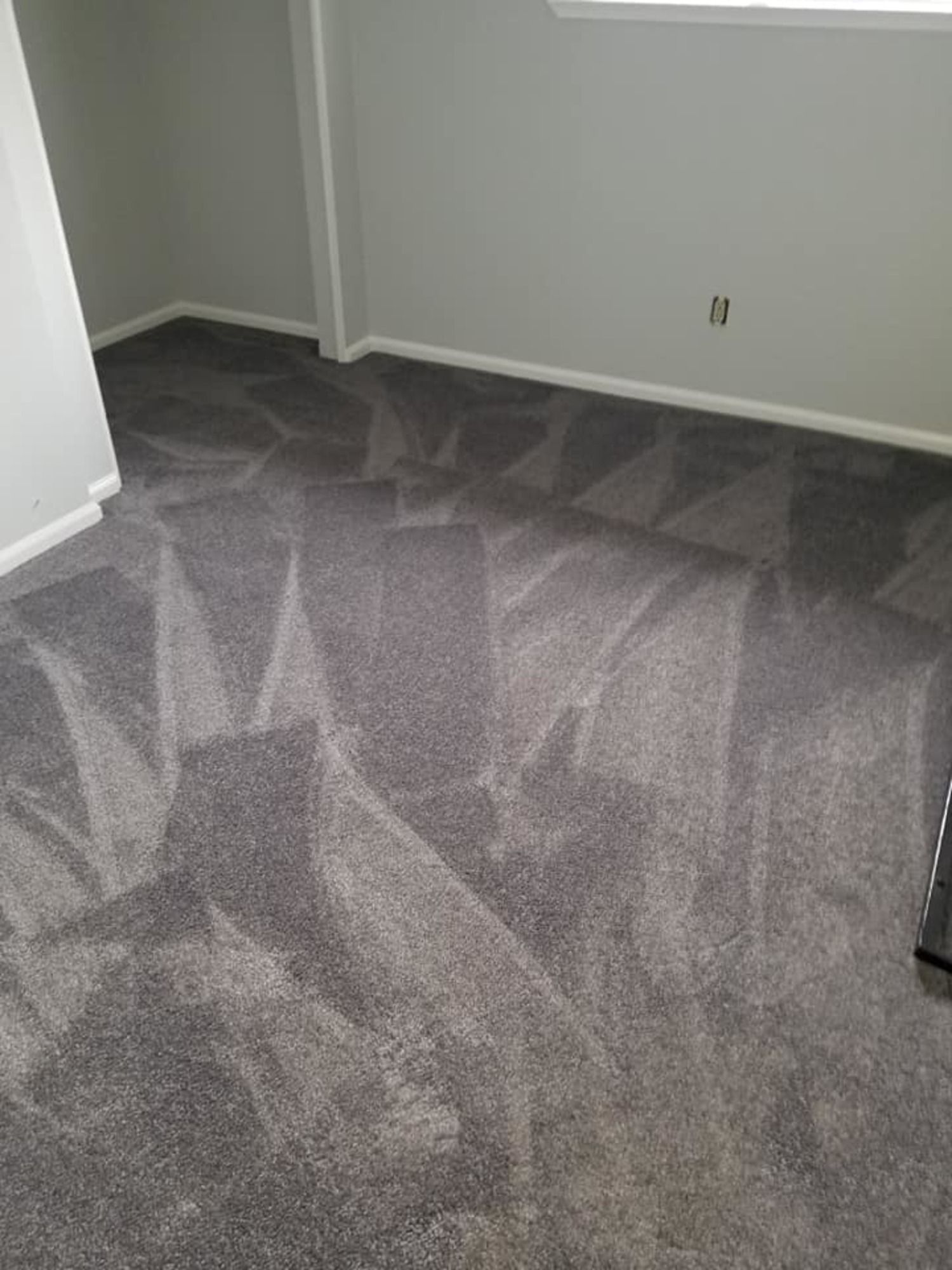 A bedroom with a gray carpeted floor and a window.