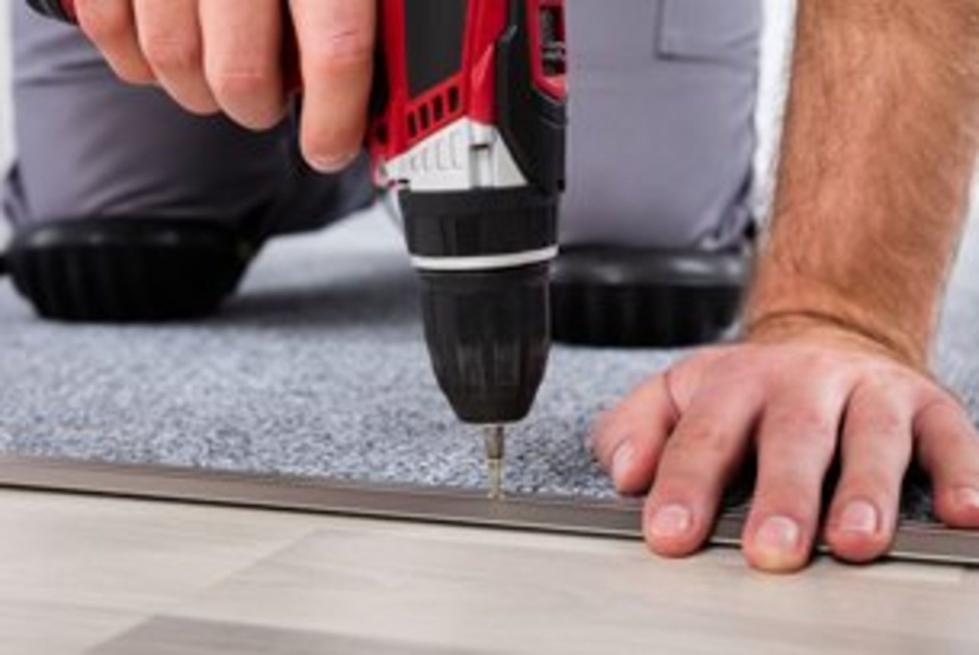 A man is using a drill to install a carpet on the floor.