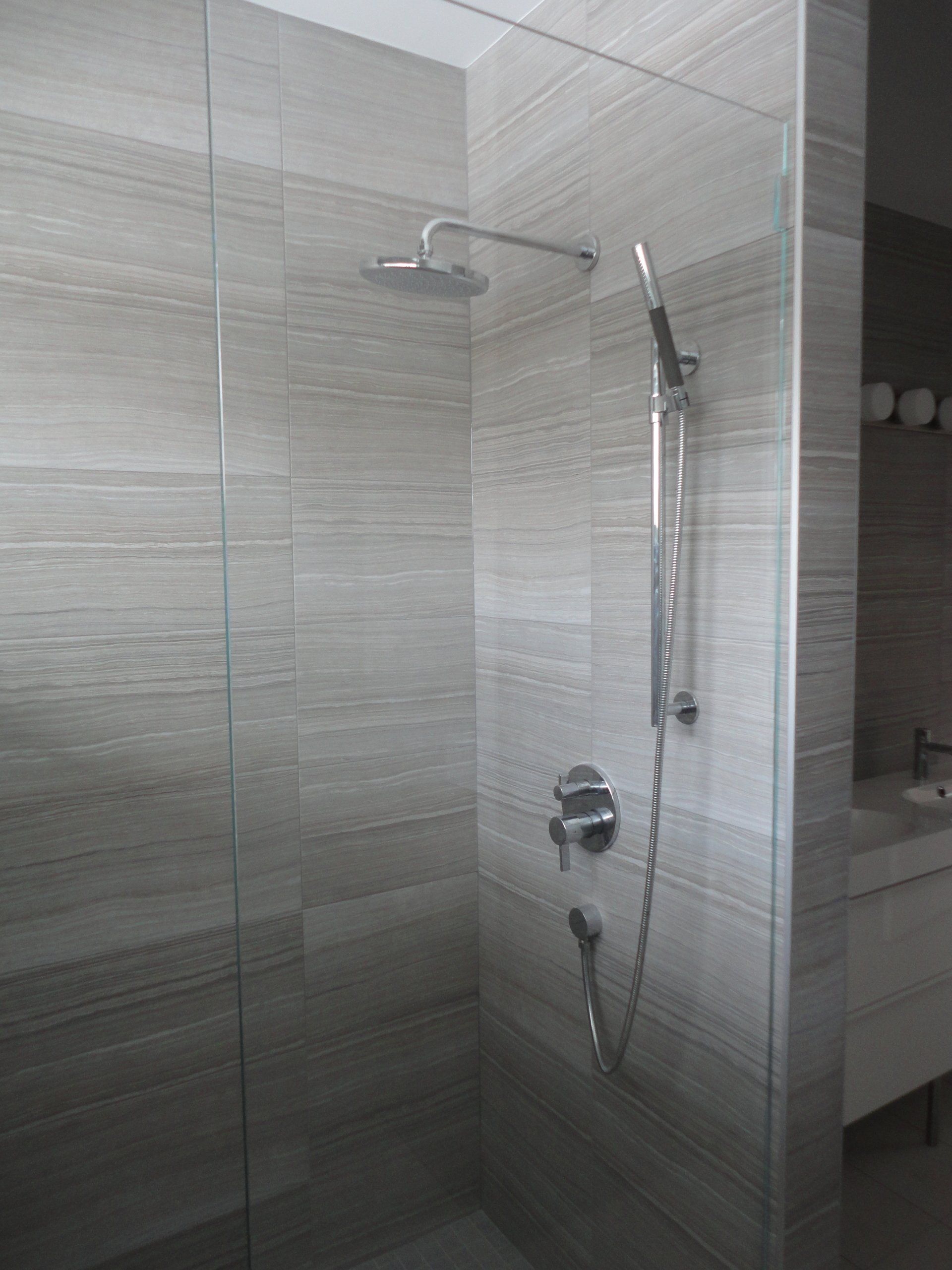 Shower stall with glass walls, gray-toned tile, and chrome shower fixtures.