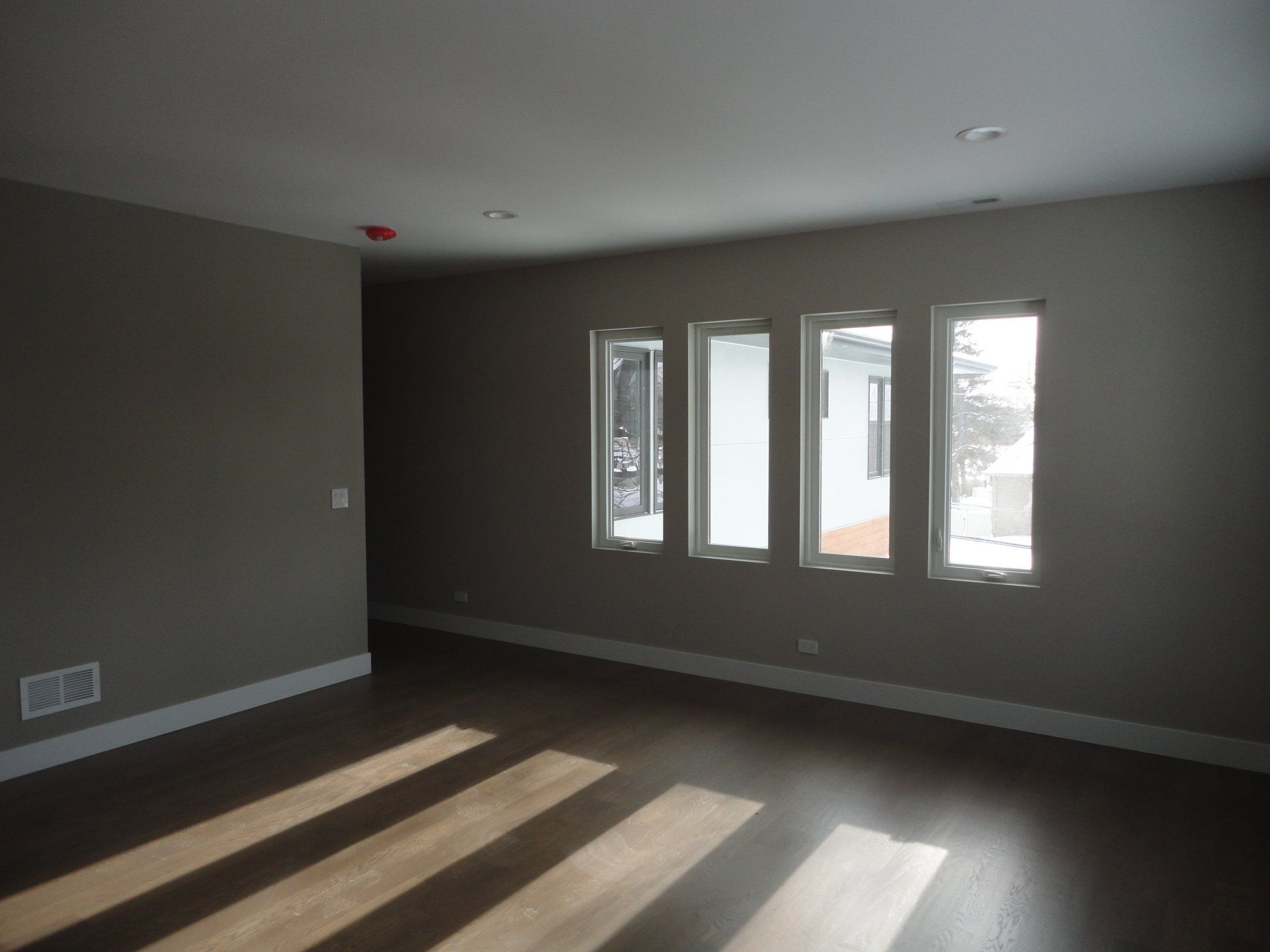 Empty room with hardwood floors and four tall windows letting in sunlight.