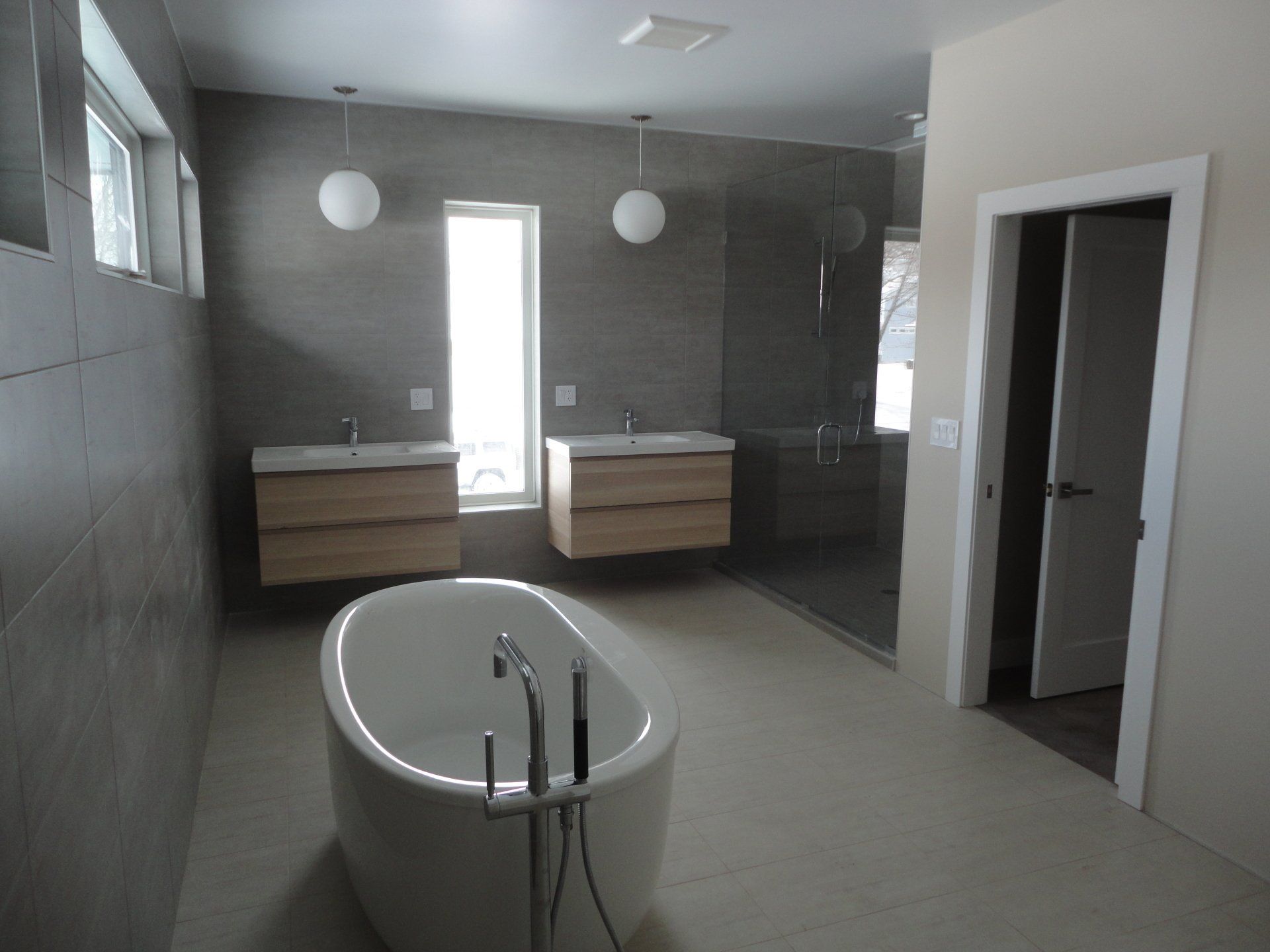 Modern bathroom with gray tile, floating wood vanities, a soaking tub, and a glass shower.