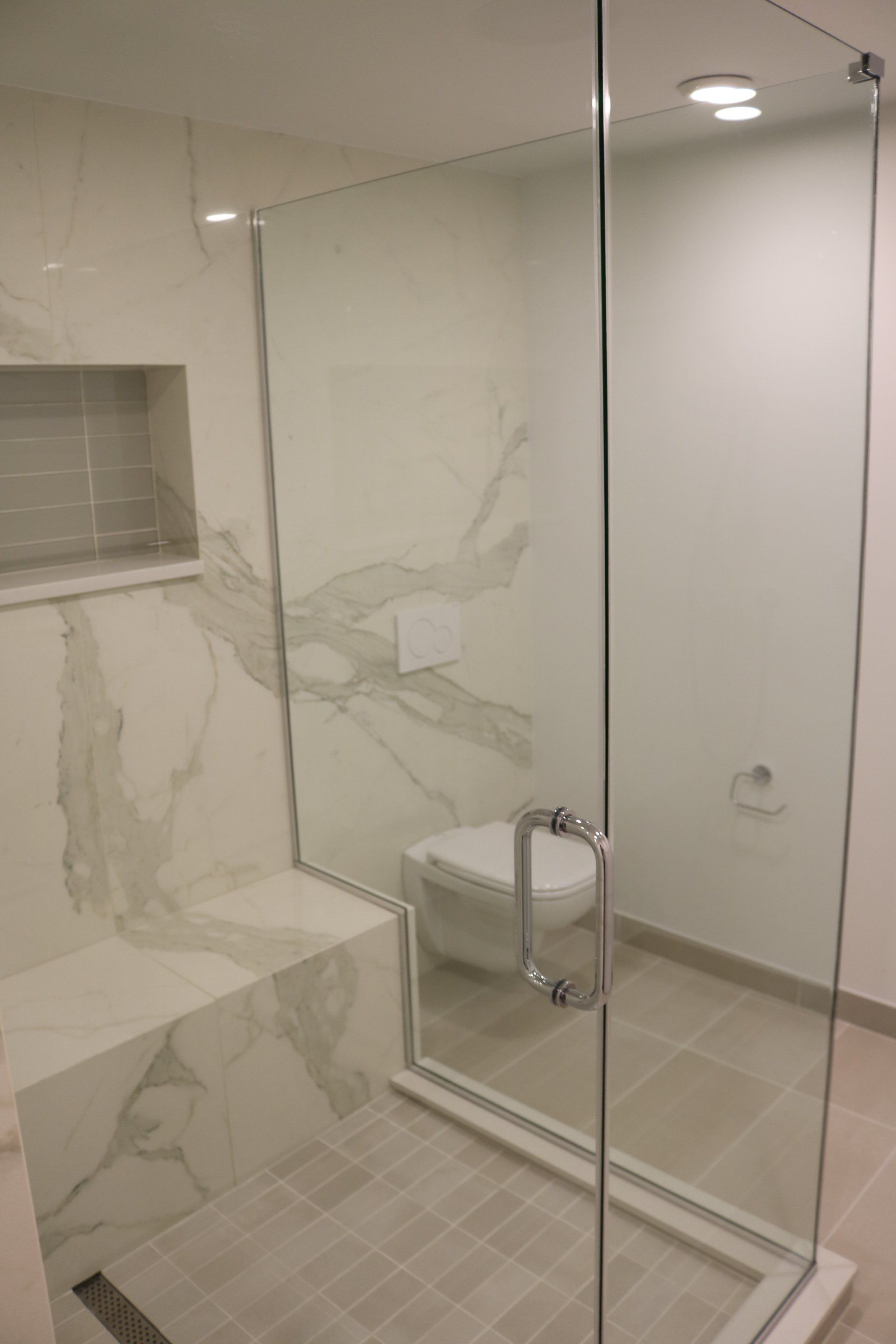 Modern bathroom with glass shower, toilet, and marble walls.