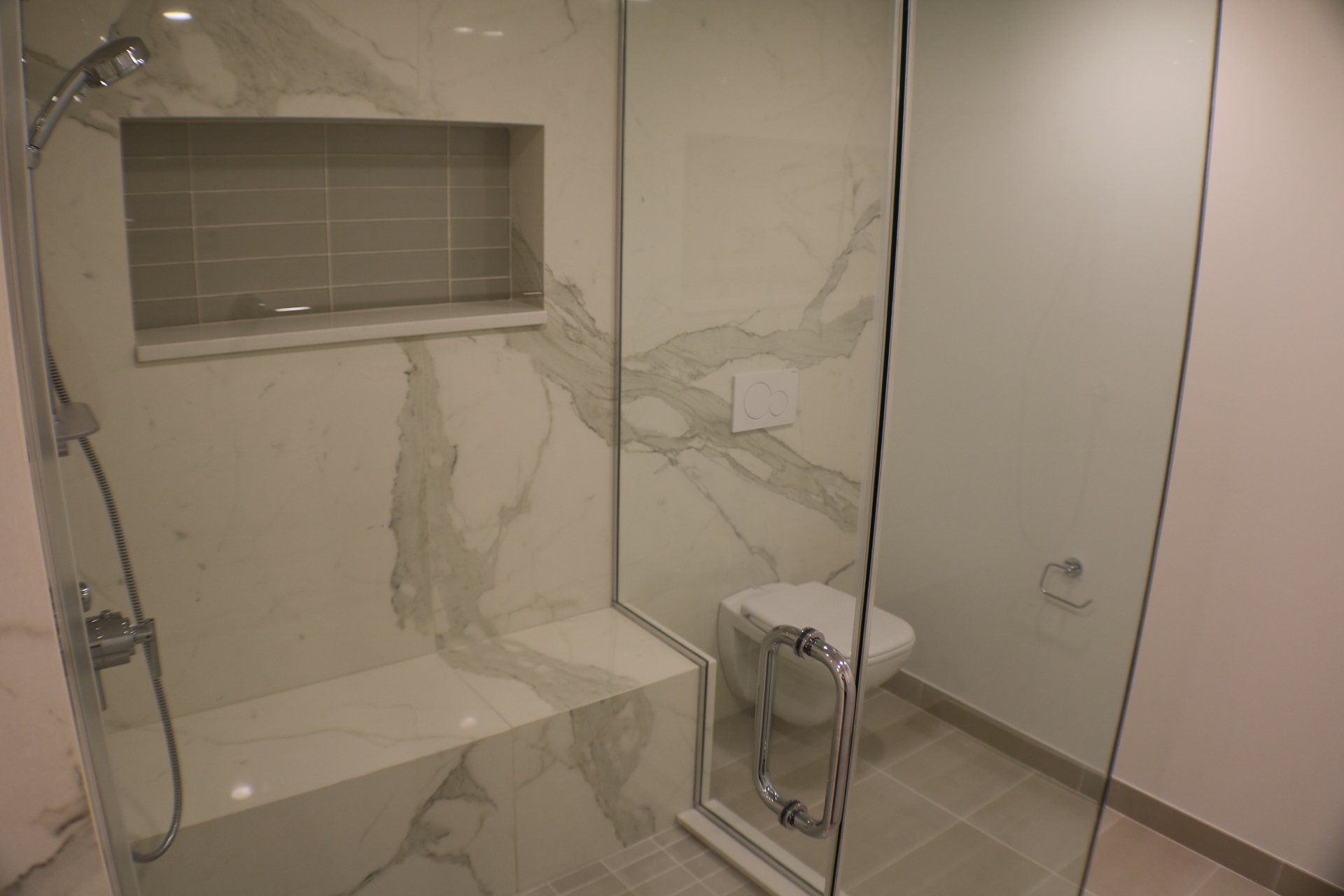 Modern bathroom with marble-look shower, built-in seat, glass door, and toilet.