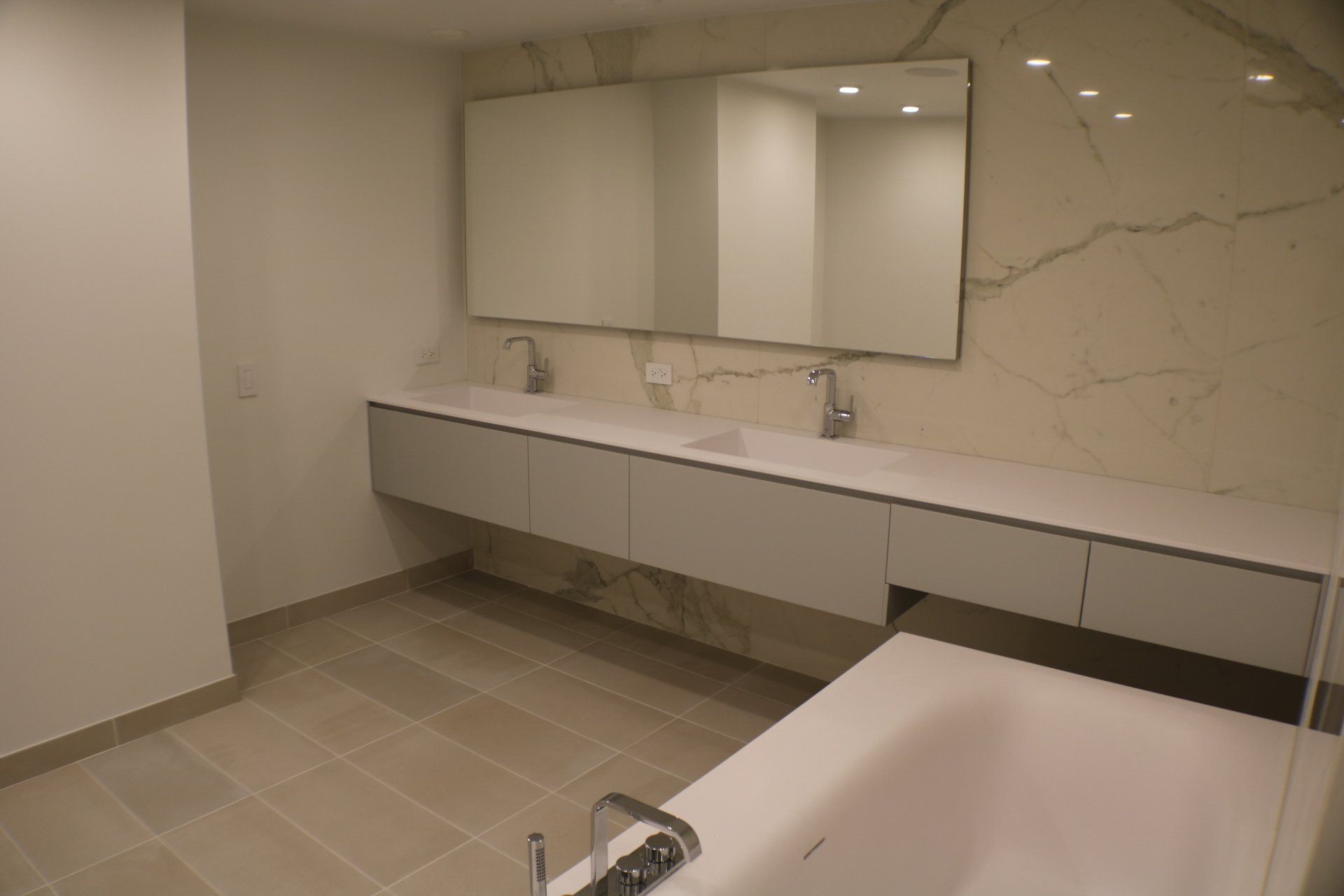 Modern bathroom with floating vanity, two sinks, large mirrors, marble accent wall, and bathtub.