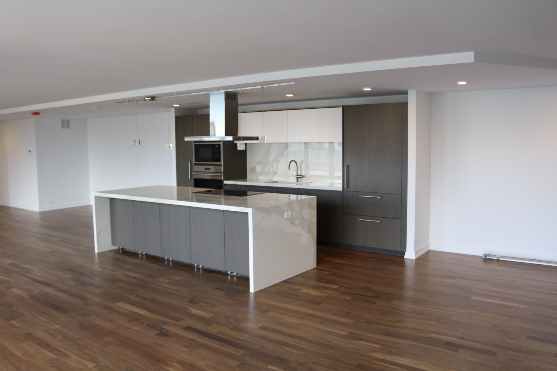 Modern kitchen with gray island and cabinetry, marble backsplash, and hardwood floor.