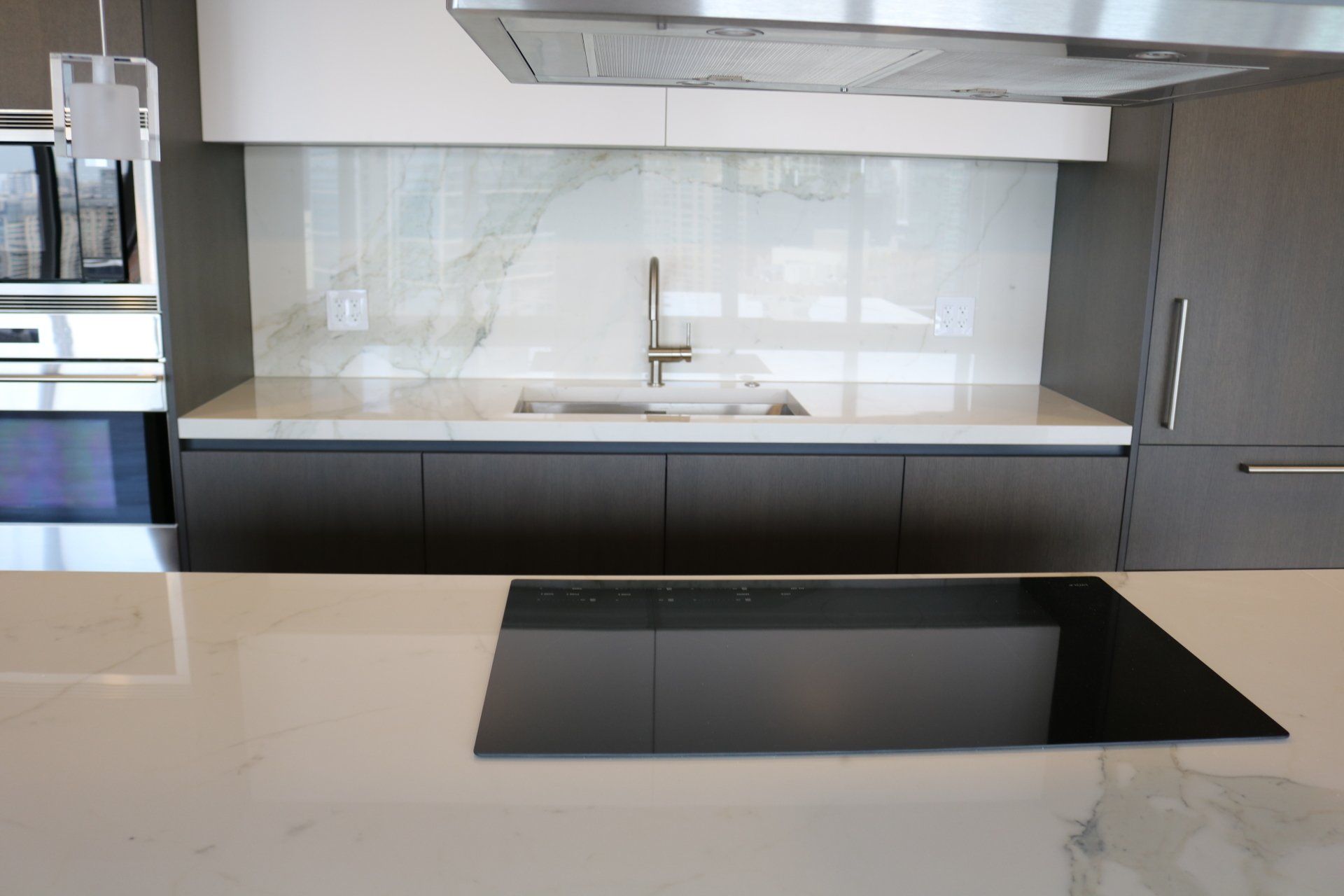 Modern kitchen with gray cabinets, white countertops, marble backsplash, and an induction cooktop.