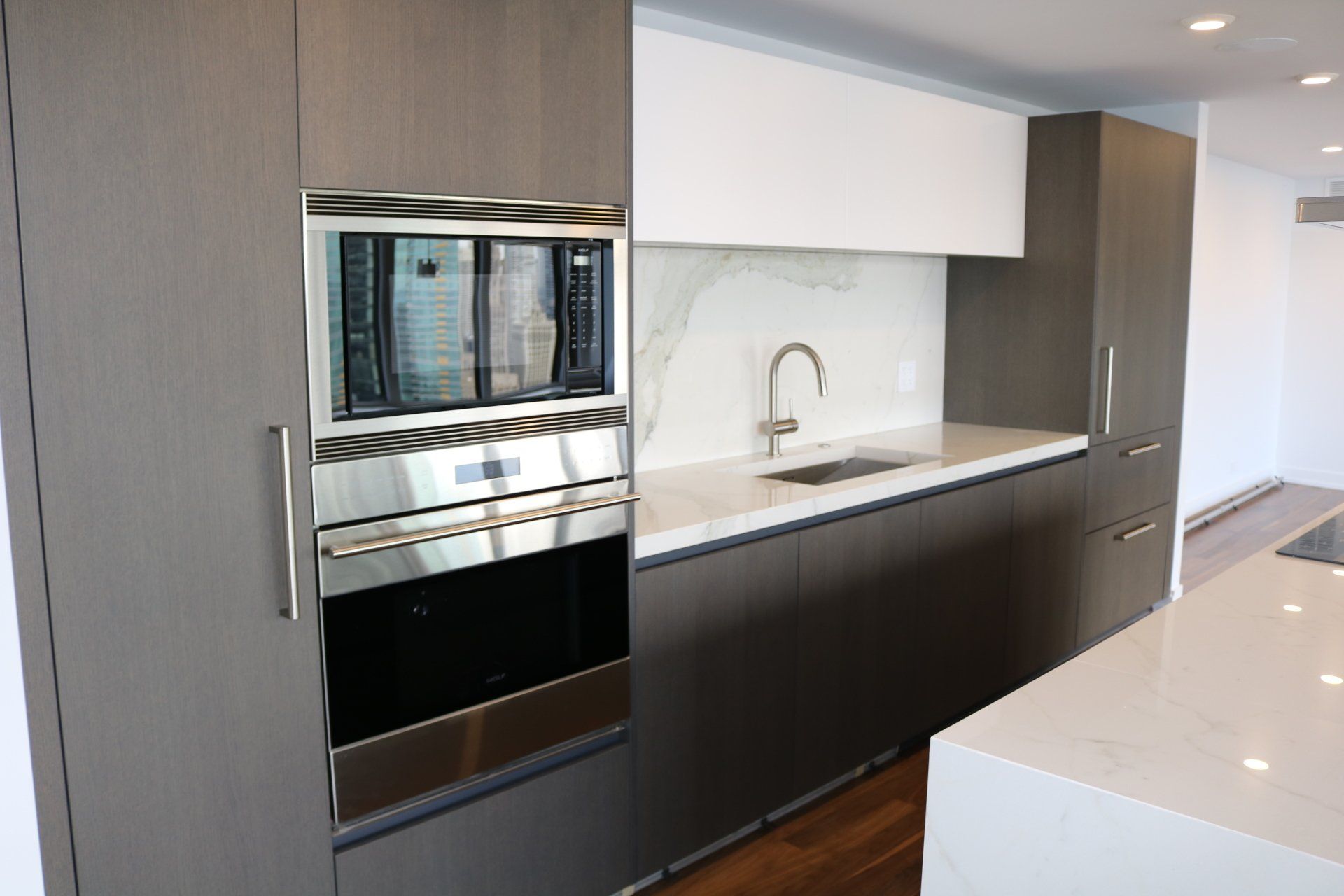 Modern kitchen with grey cabinets, stainless steel appliances, and white countertops.