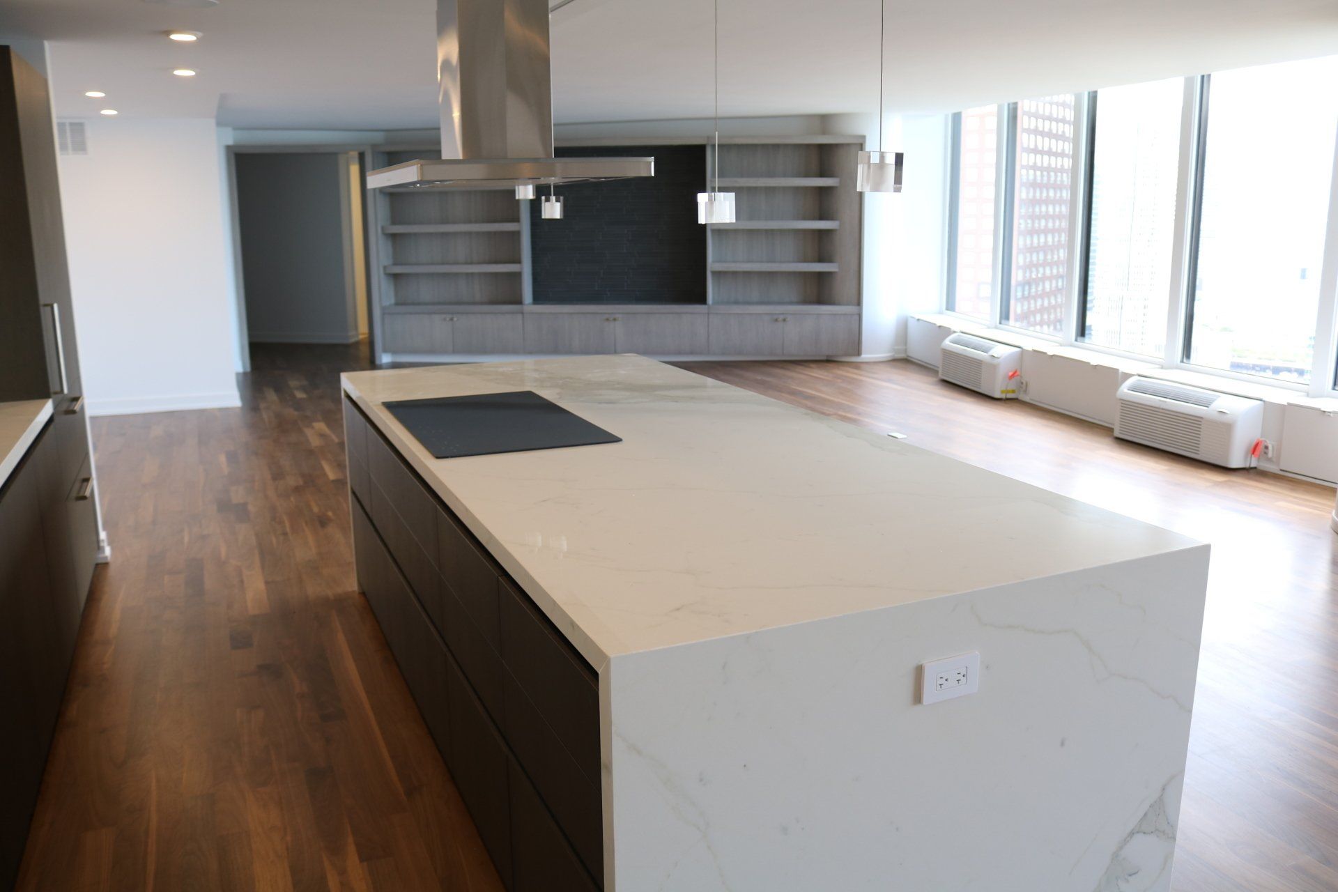 Modern kitchen with white countertop island, dark cabinets, and hardwood floors.