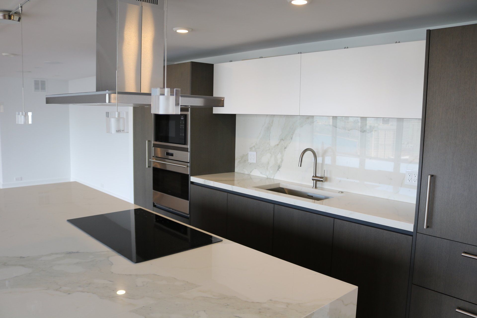 Modern kitchen with island and built-in appliances; white and dark gray cabinetry, stainless steel range hood.