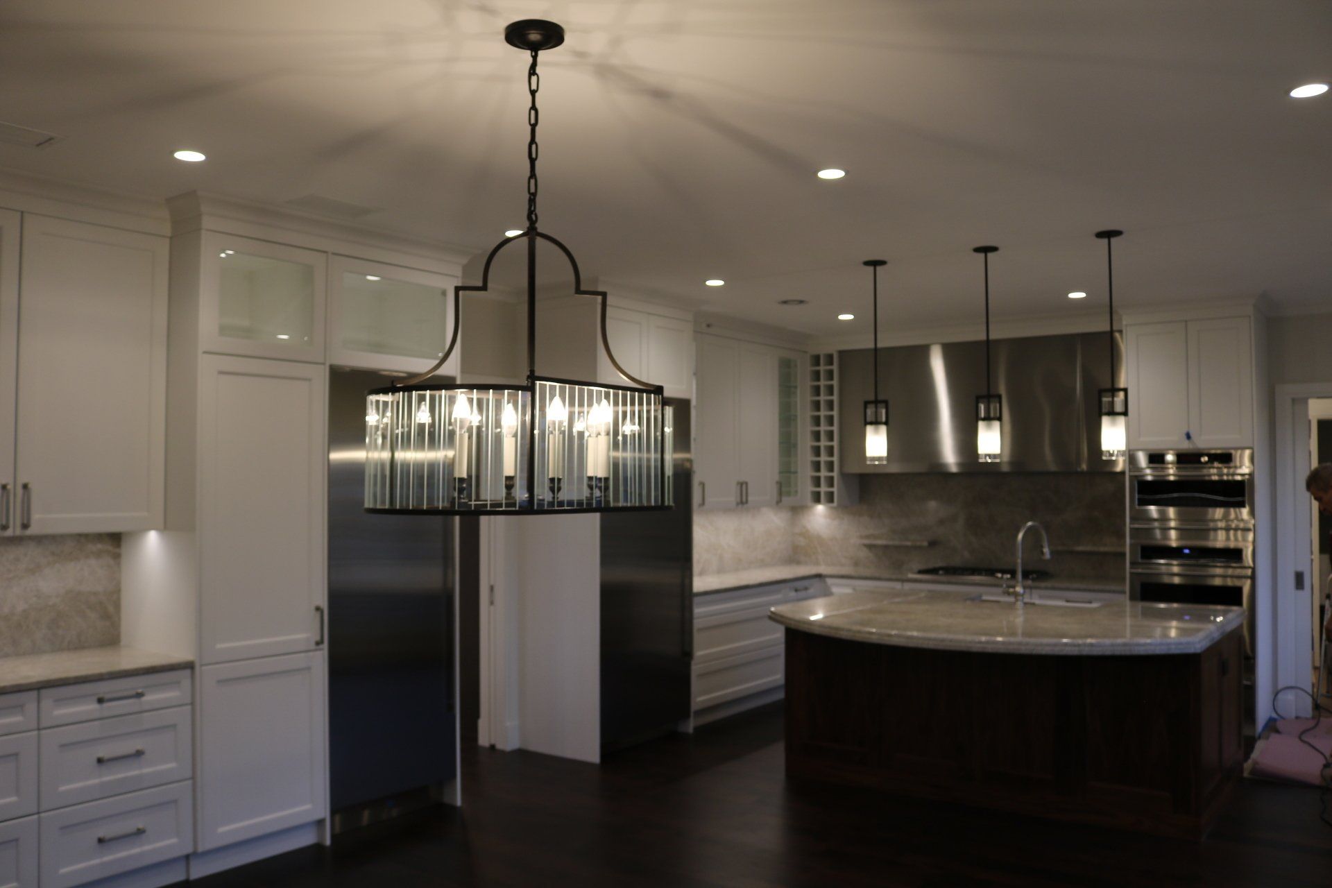 Modern kitchen with white cabinets, dark island, and large chandelier.