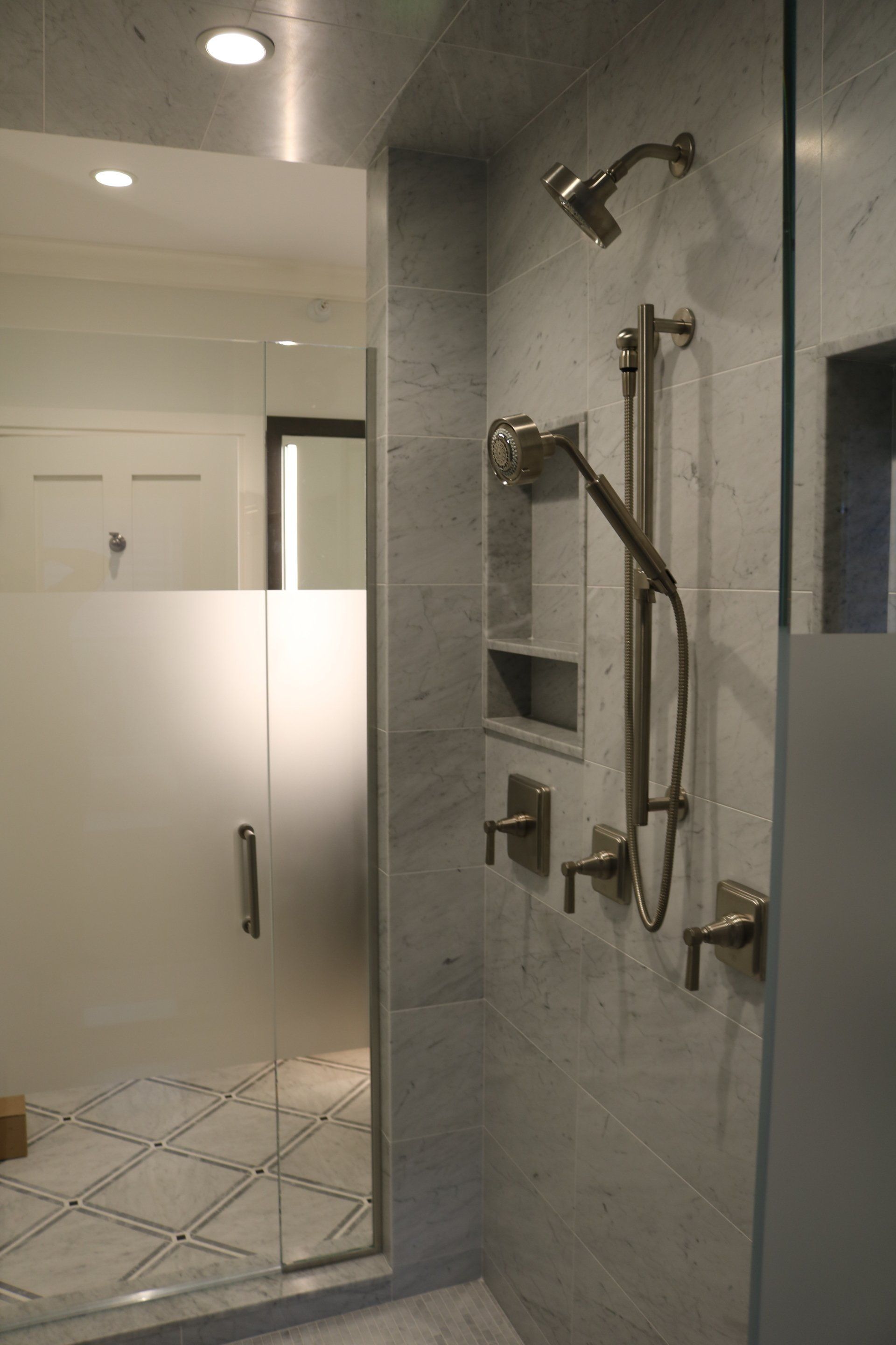 A modern bathroom with a tiled shower, glass door, and brushed nickel fixtures.
