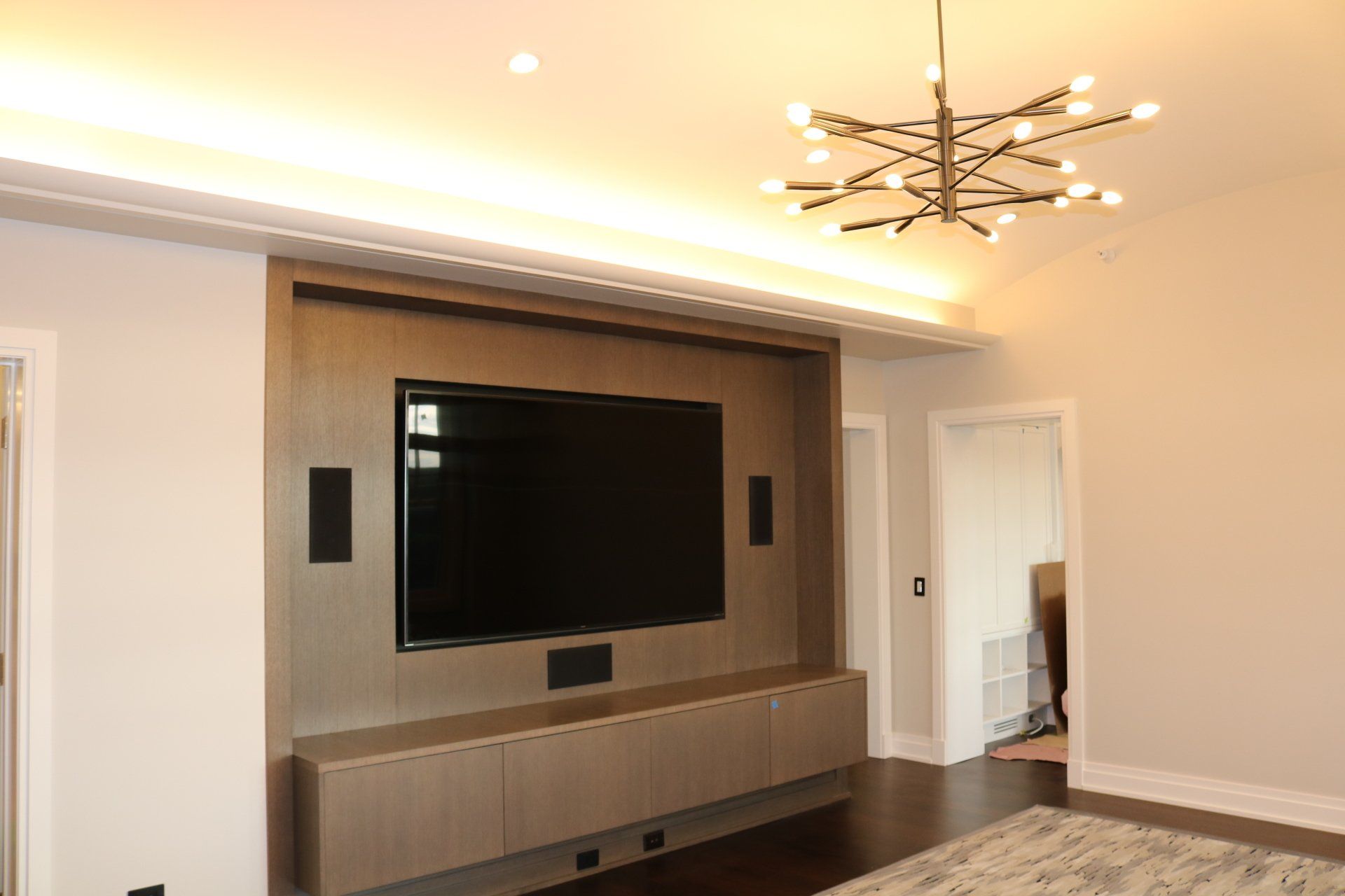 Living room with a large-screen TV, mounted speakers, and a modern chandelier.