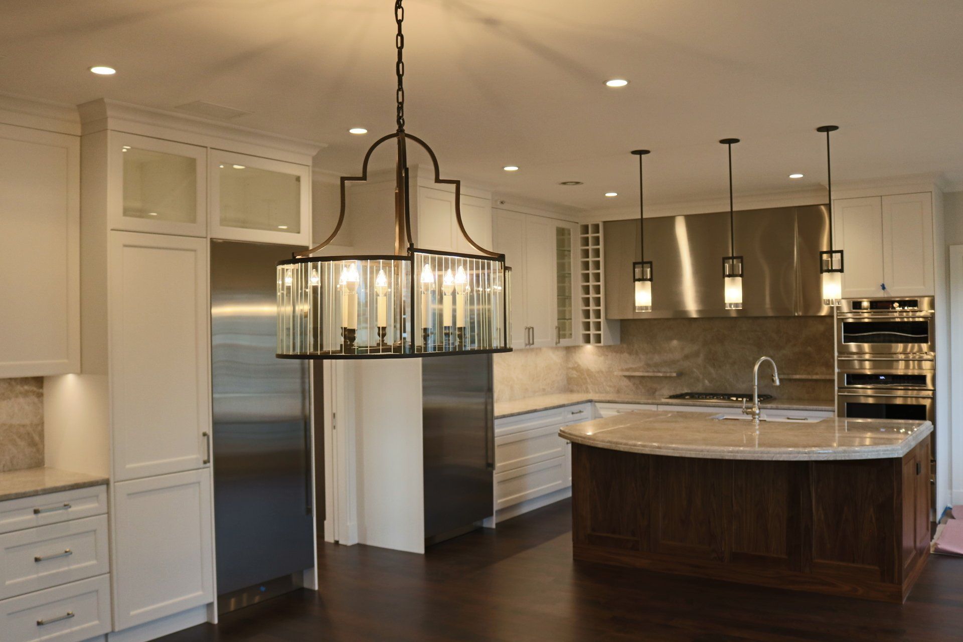 Upscale kitchen: white cabinets, dark wood island, stainless steel appliances, chandelier, recessed lighting.