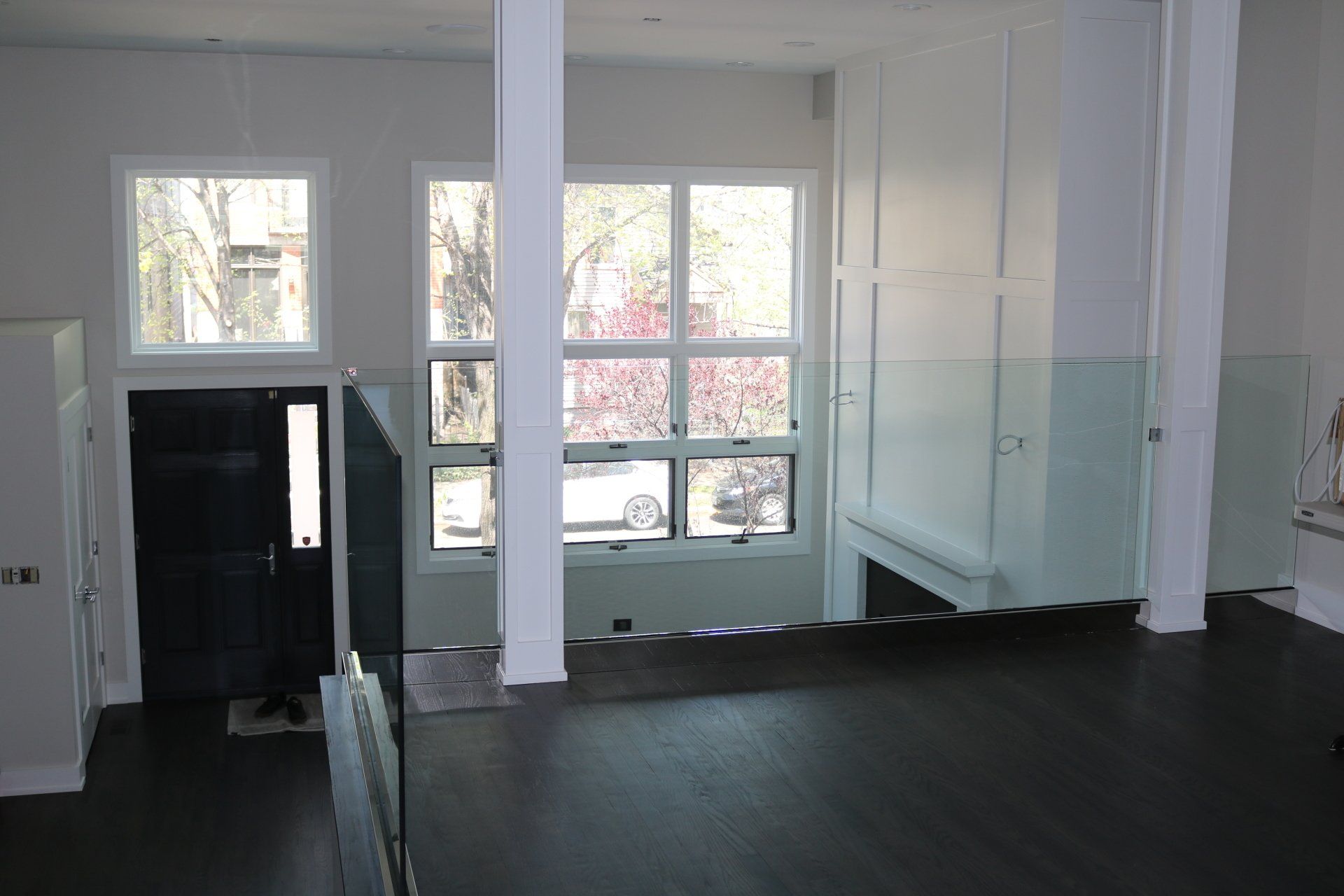 Interior view of a bright, modern home with dark floors, large windows, and white walls, including support pillars.