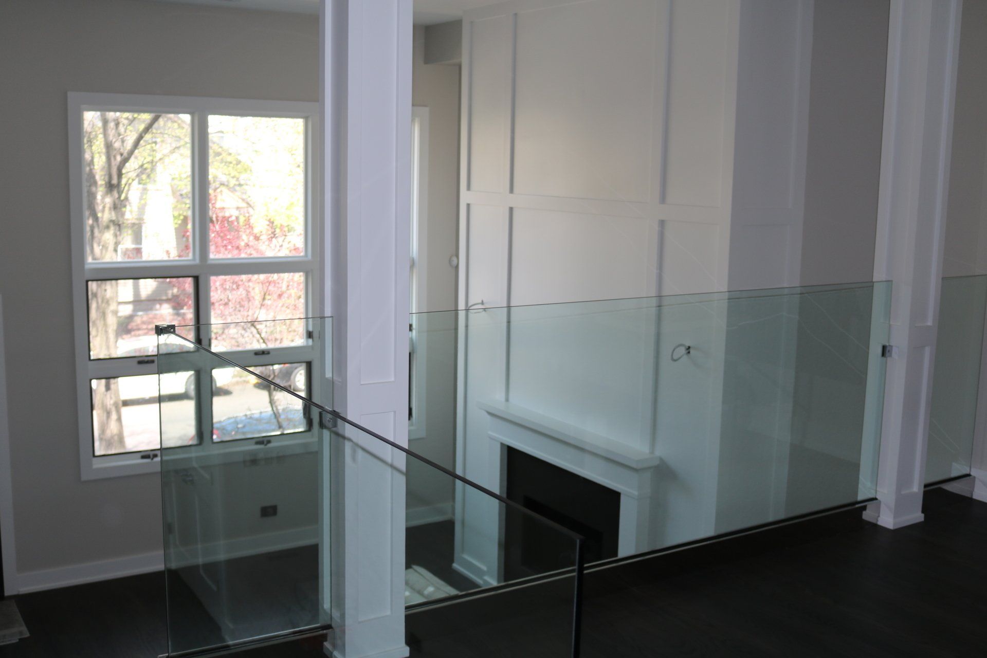 Interior view of a modern home with a glass railing, white walls, a fireplace, and a window looking out to trees.
