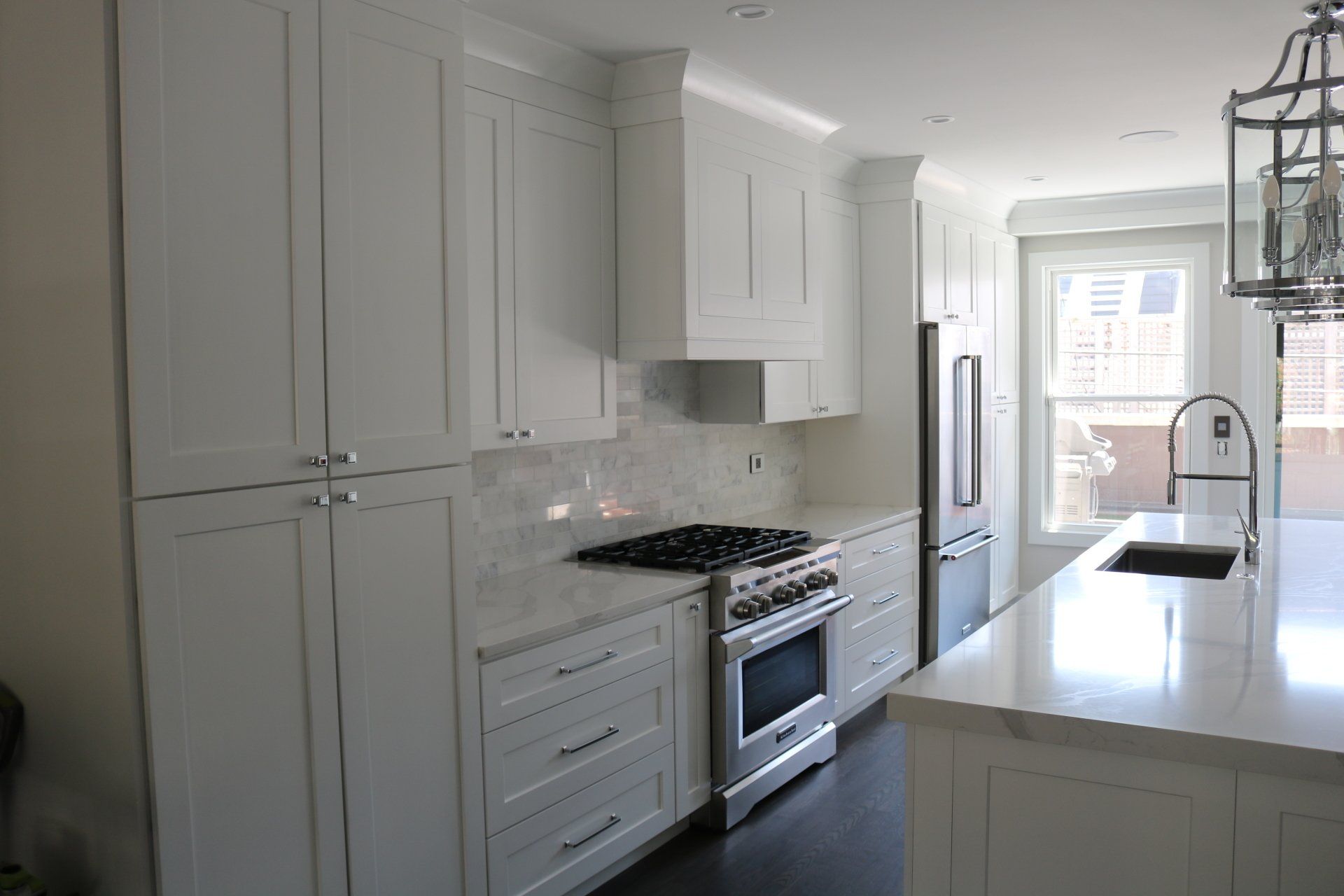 White kitchen with stainless steel appliances, marble countertops, and a large window.