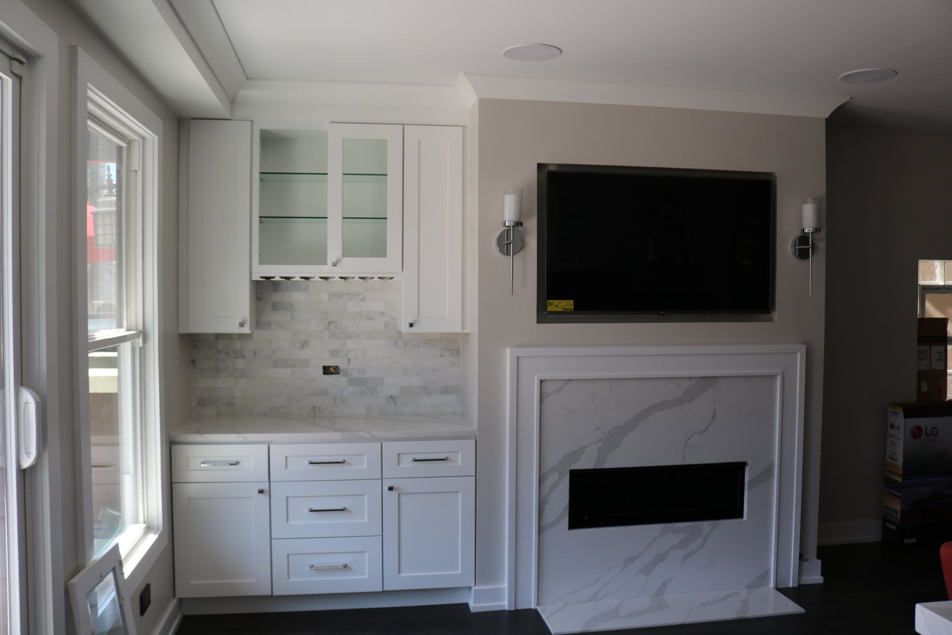 White cabinets and marble fireplace with TV mounted on wall, with glass cabinets above a tiled backsplash.