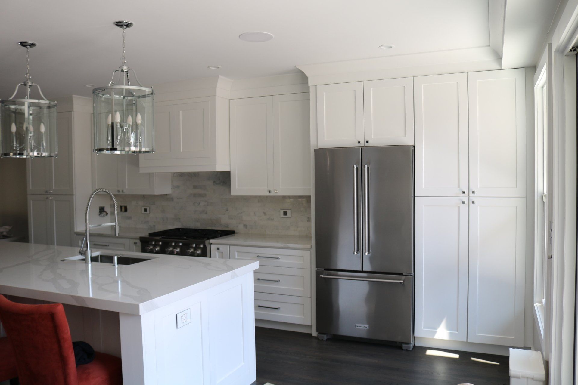 White kitchen with stainless steel fridge, island, pendant lights, and white cabinets.