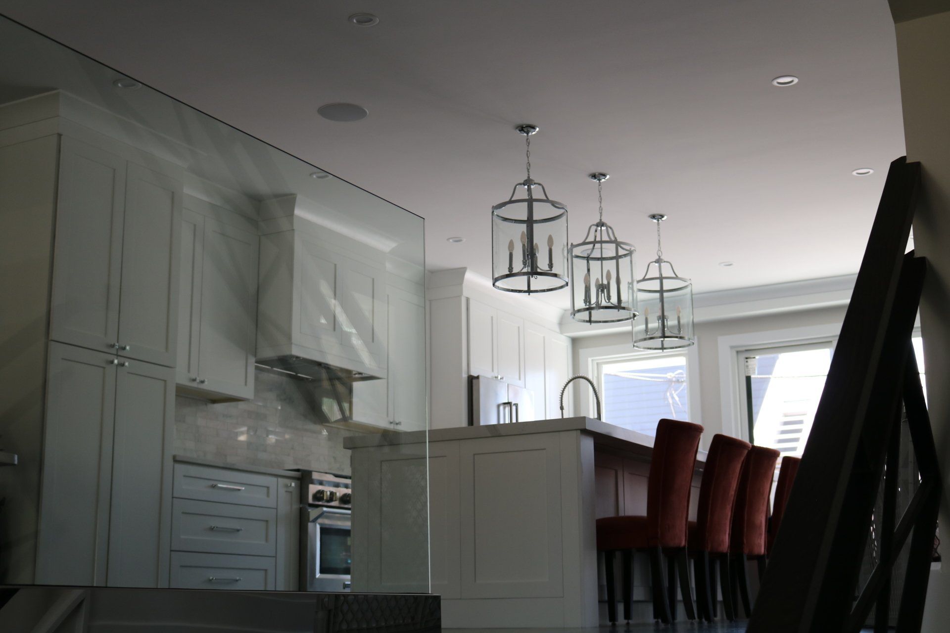 White kitchen with island, pendant lights, range hood. Red barstools, and cabinets visible.