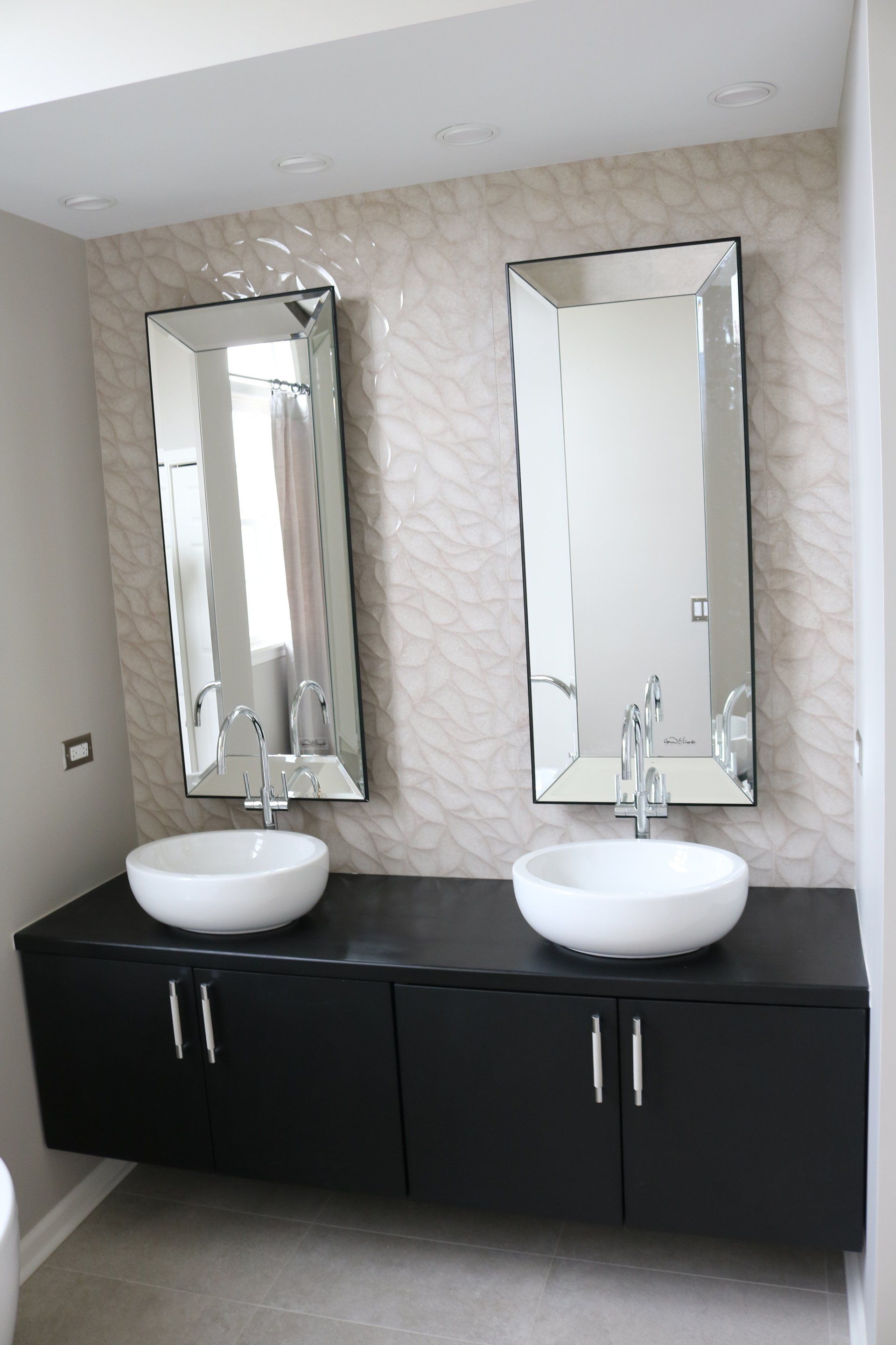 Bathroom with floating black vanity, two vessel sinks, beveled mirrors, and patterned wallpaper.