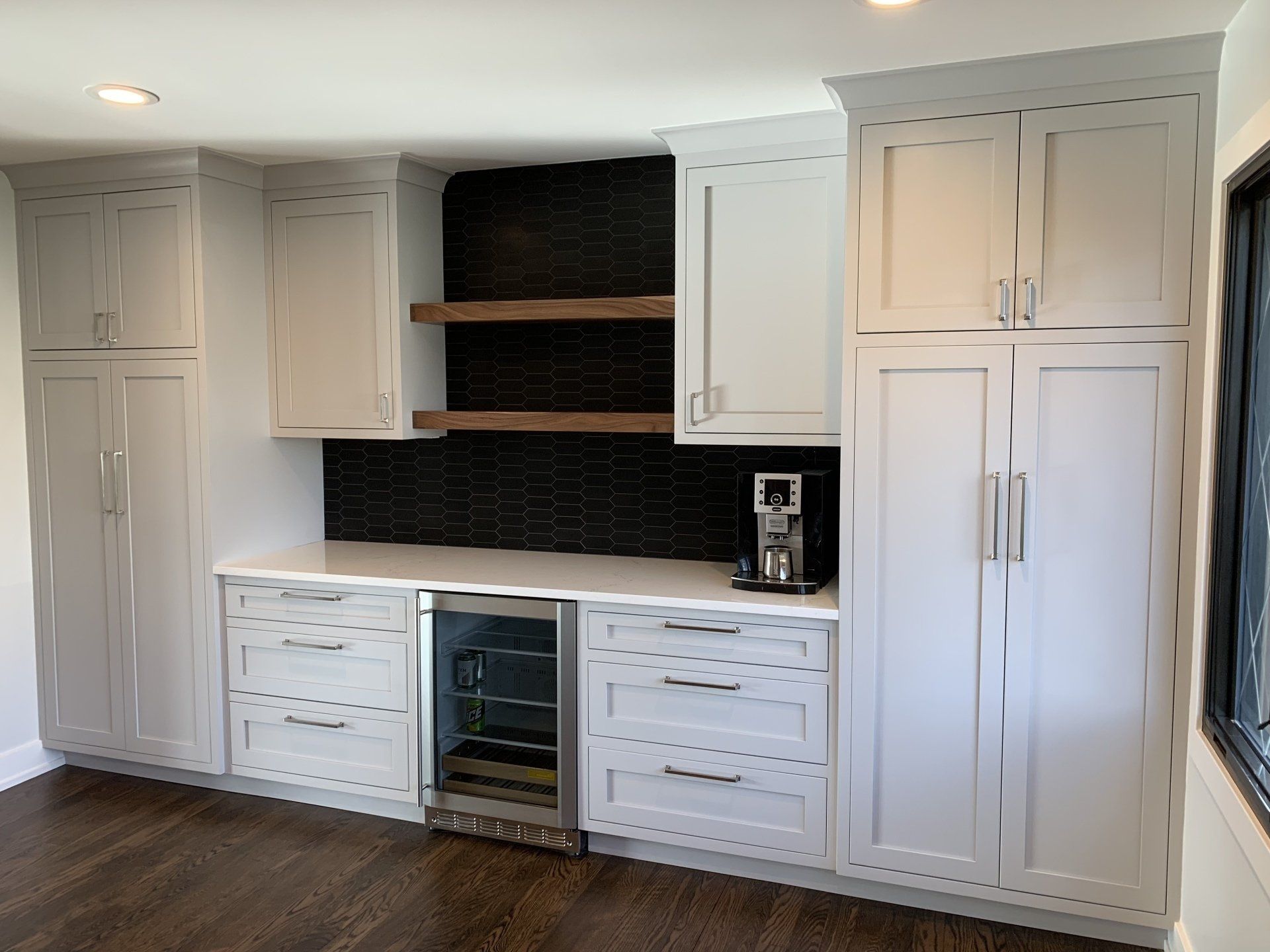 Light gray kitchen cabinetry with a wine fridge and coffee maker, dark wood accents.